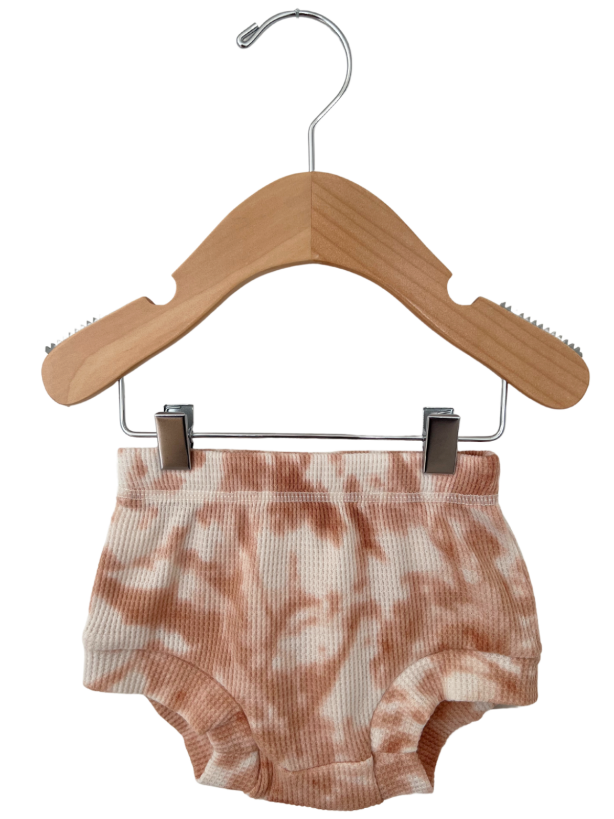 Pink tie-dye baby shorts hanging on a wooden hanger against a white background.