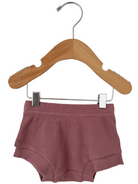 Pink ribbed shorts hanging on a wooden hanger against a white background.