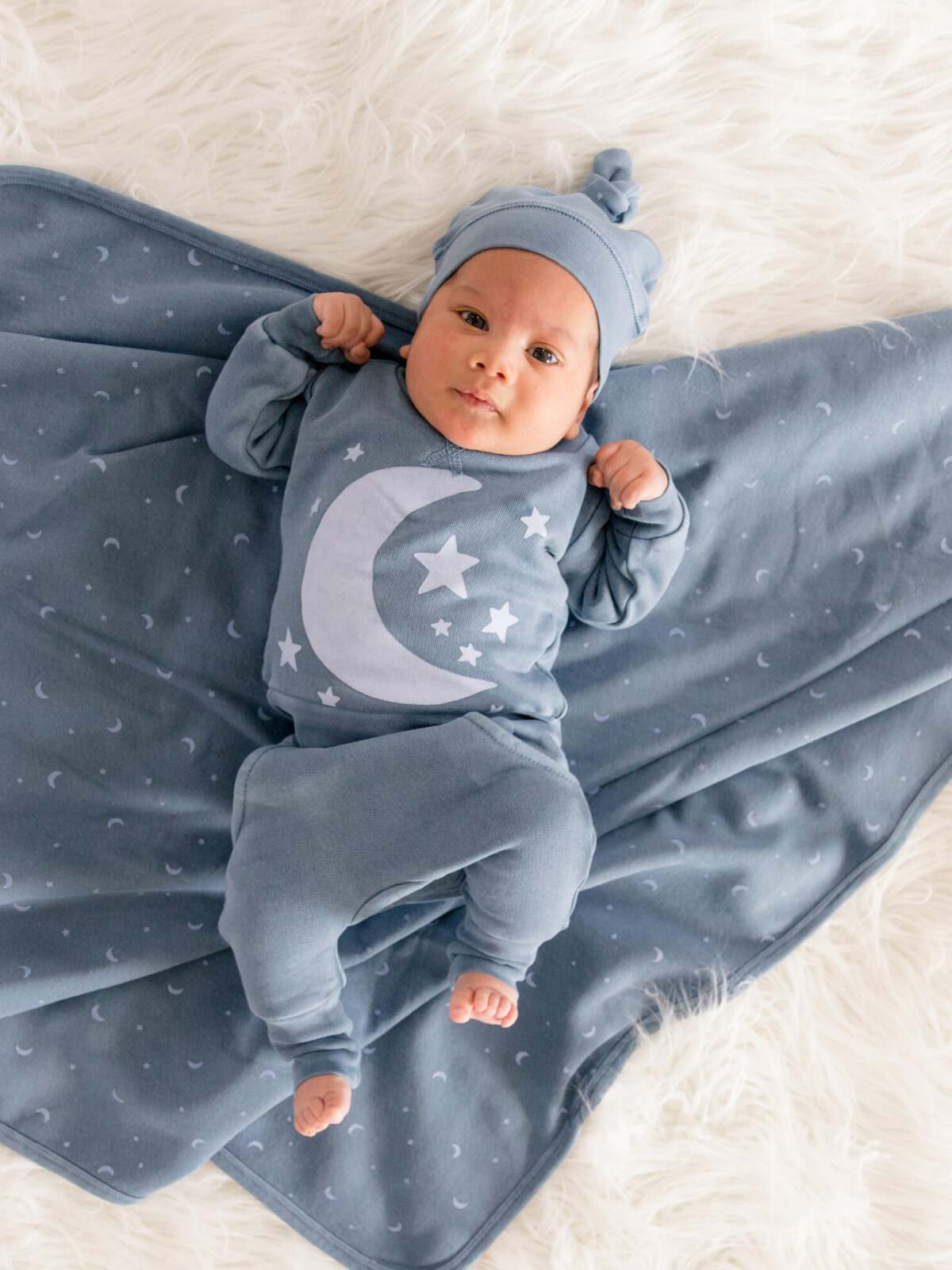 Infant dressed in blue moon and star pajamas, lying on a soft, fluffy blanket.
