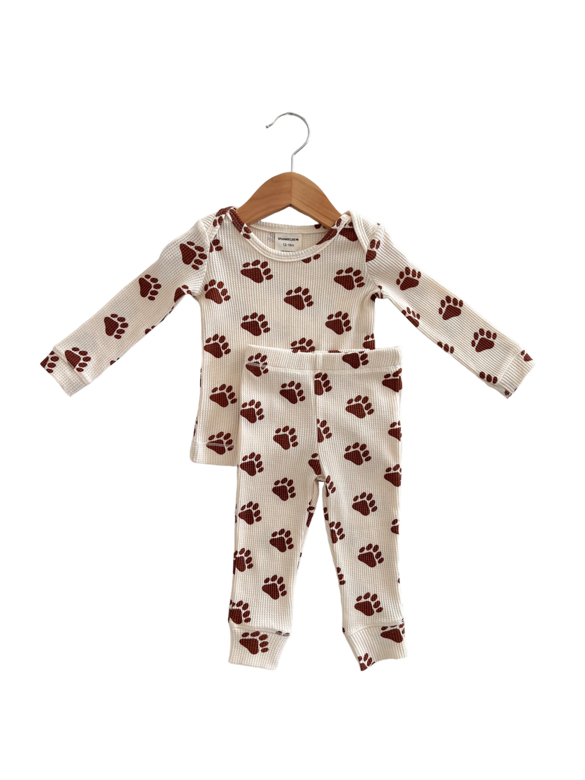 Brown paw print children's pajama set, featuring a long-sleeve top and matching pants, hung on a wooden hanger.