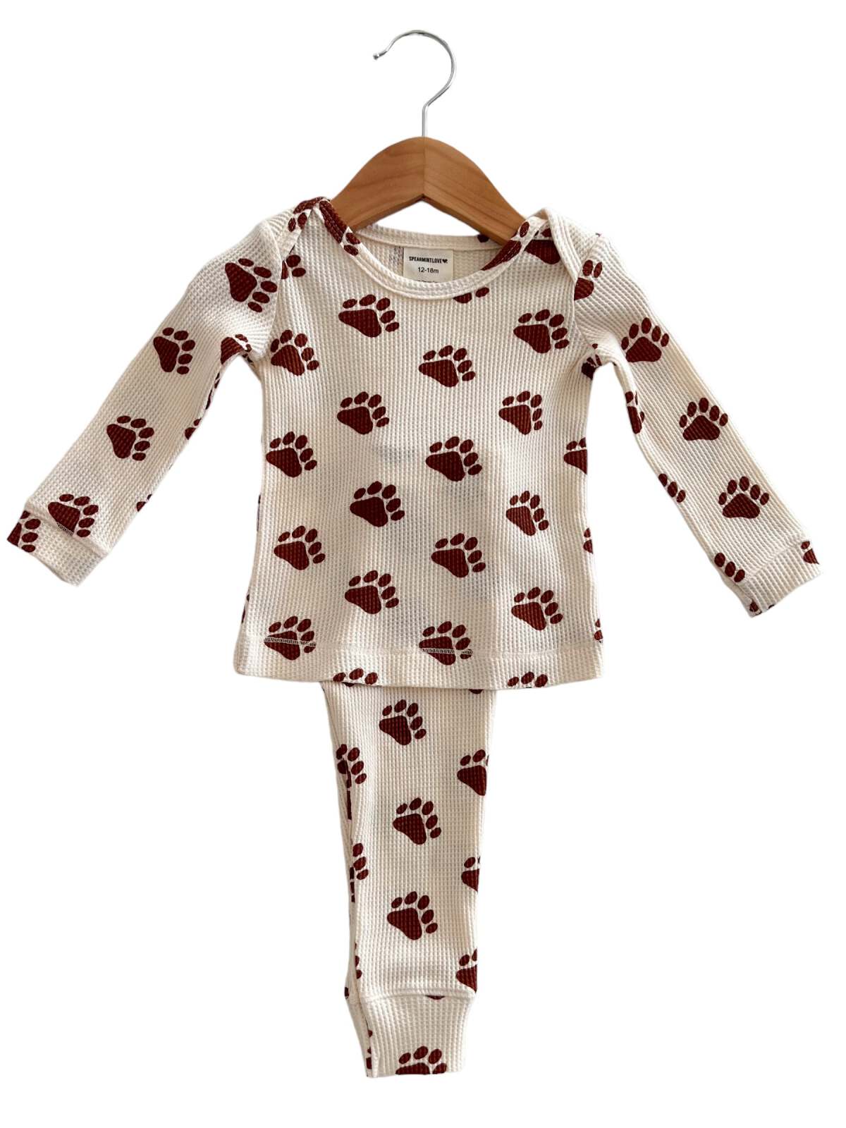 Cream pajama set with maroon bear paw prints, hanging on a wooden hanger. Suitable for infants aged 12-18 months.