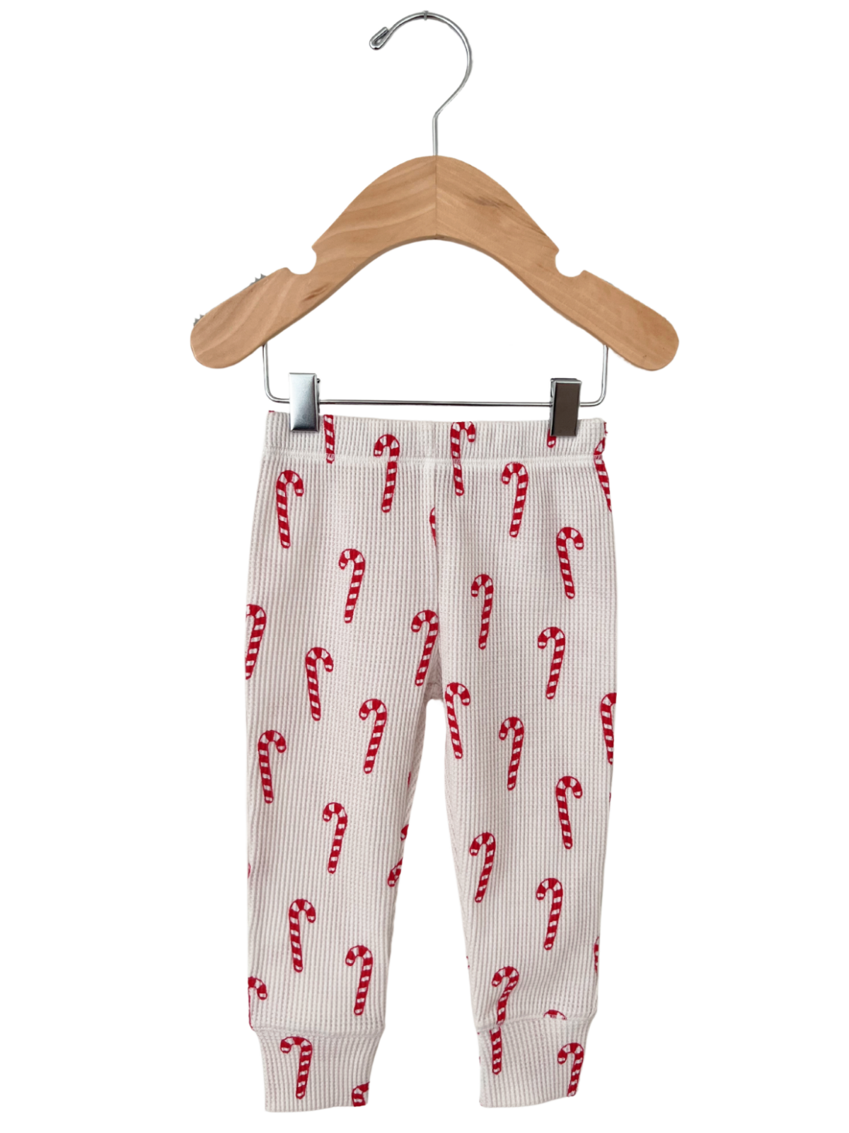 Kid's ribbed leggings with red and white candy cane pattern, displayed on a wooden hanger.