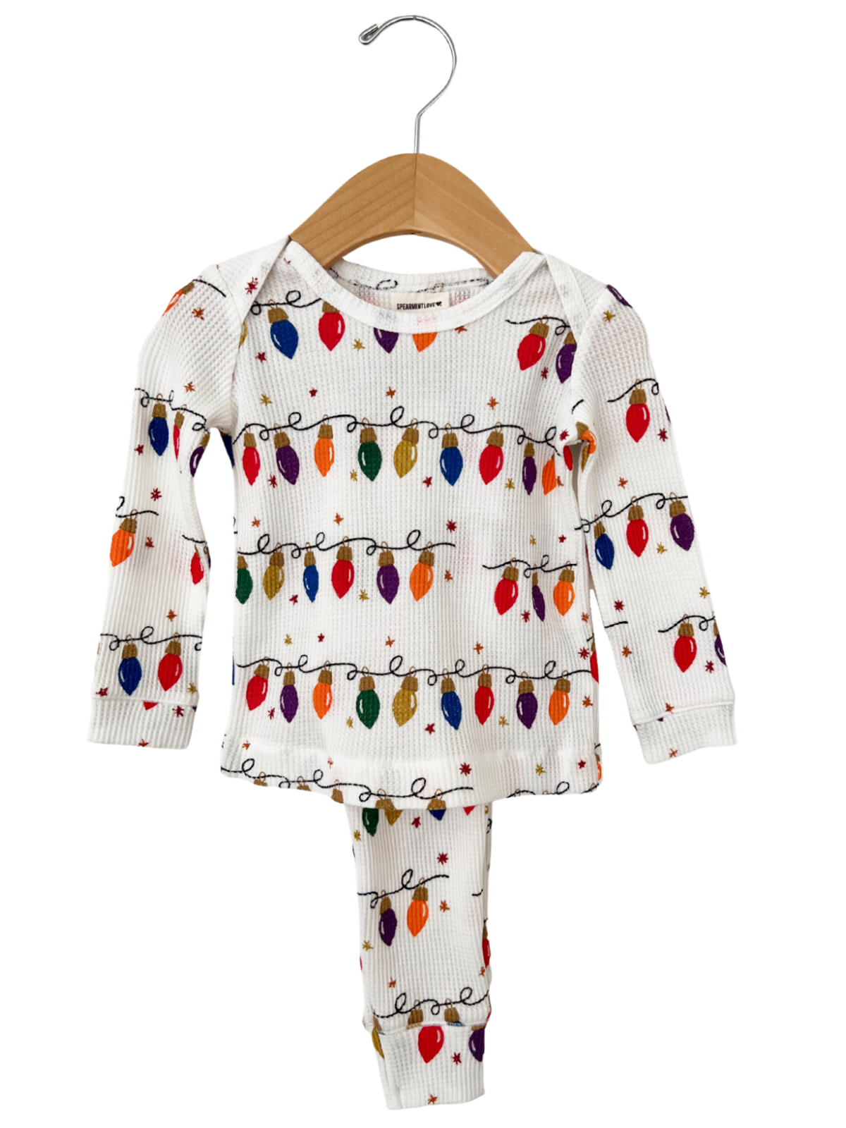 White kids' pajamas with colorful Christmas lights and stars pattern, hanging on a wooden hanger.
