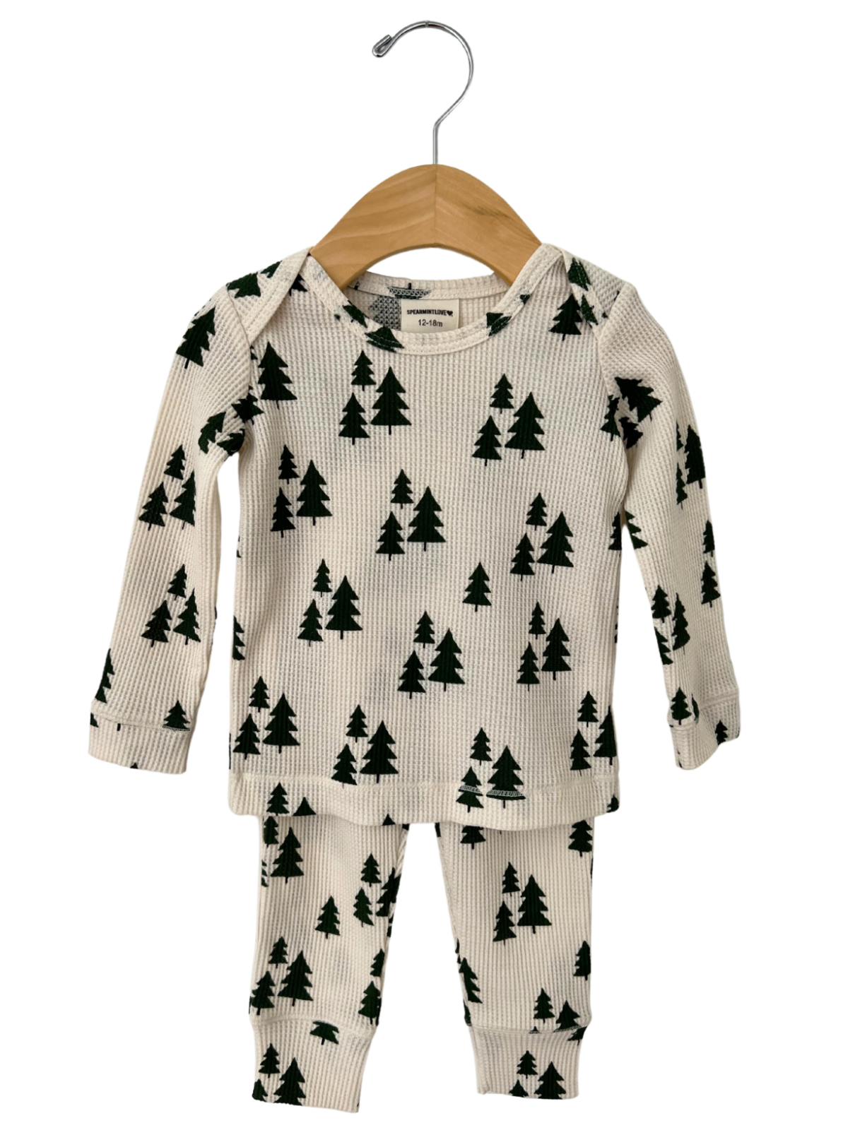 Kids' cream-colored pajamas with a green tree pattern, hanging on a wooden hanger.
