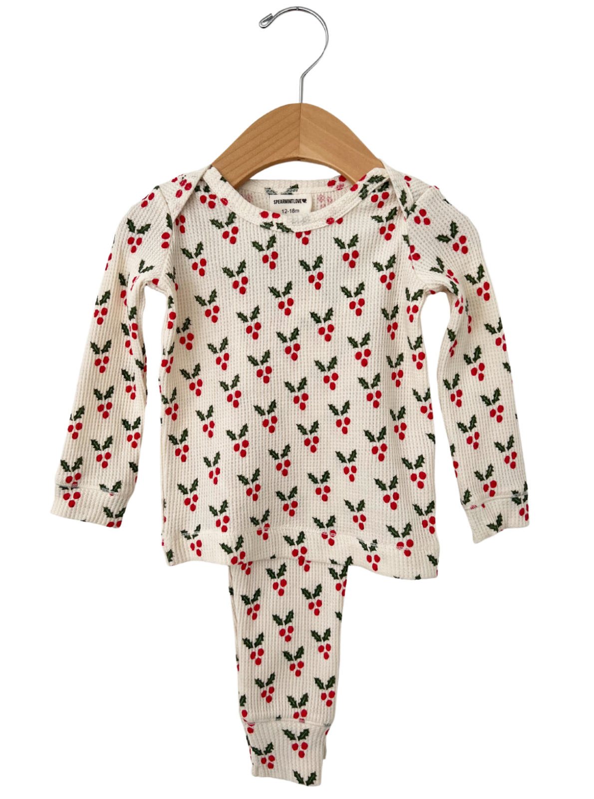 Christmas-themed children's pajama set with red berries and green leaves, hanging on a wooden hanger.