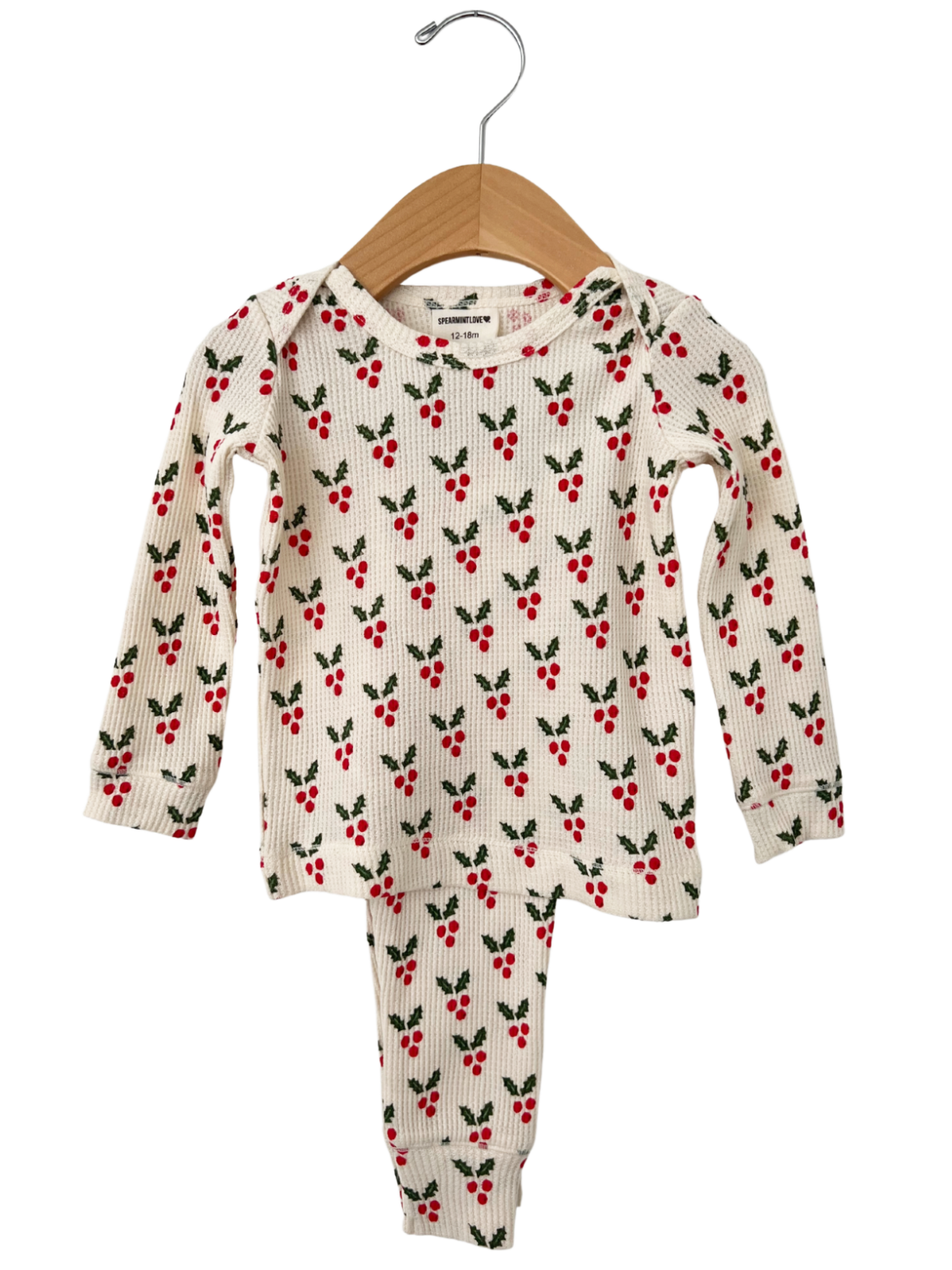 Christmas-themed children's pajama set with red berries and green leaves, hanging on a wooden hanger.