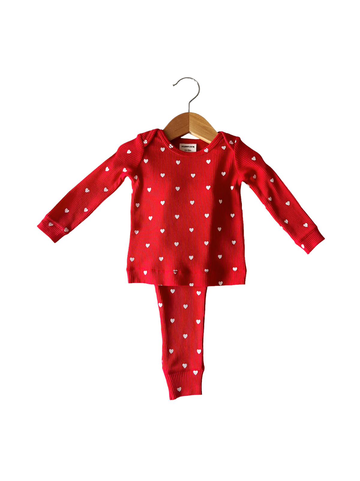 Red children's pajama set featuring white heart patterns, hanging on a wooden hanger against a white background.