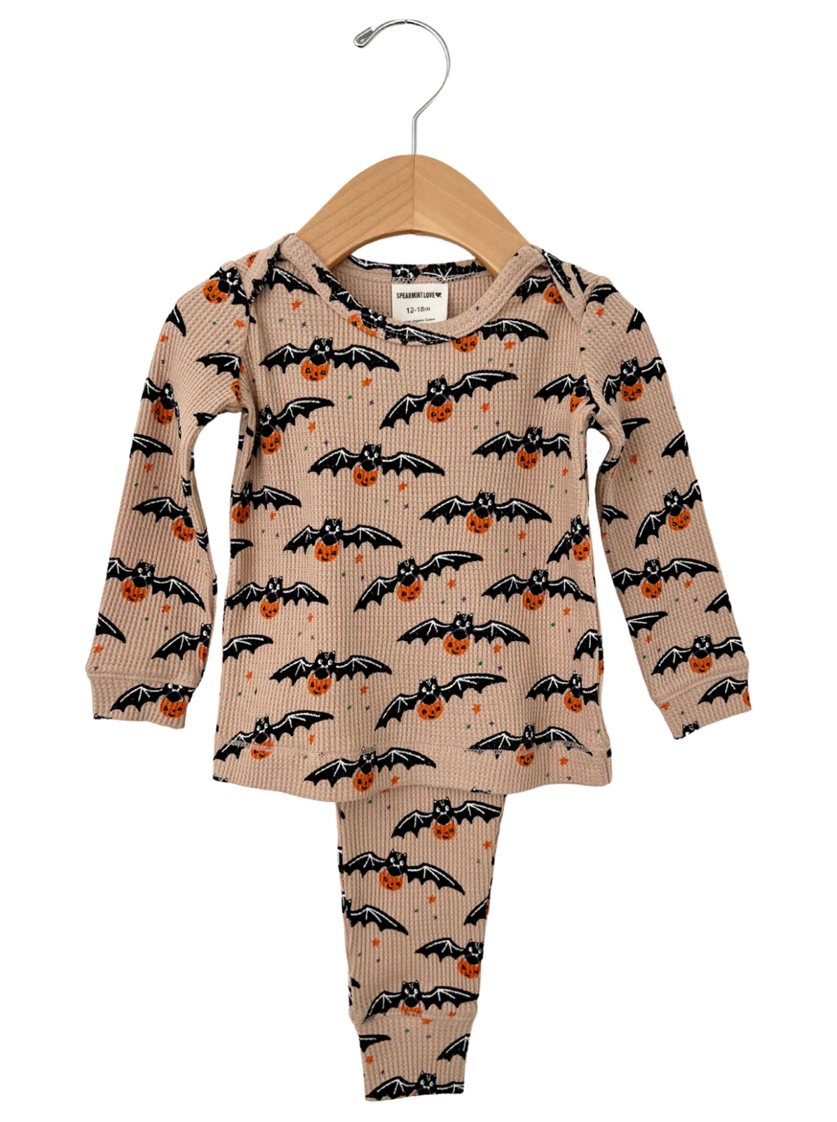Tan bat and pumpkin patterned children's pajama set hanging on a wooden hanger.