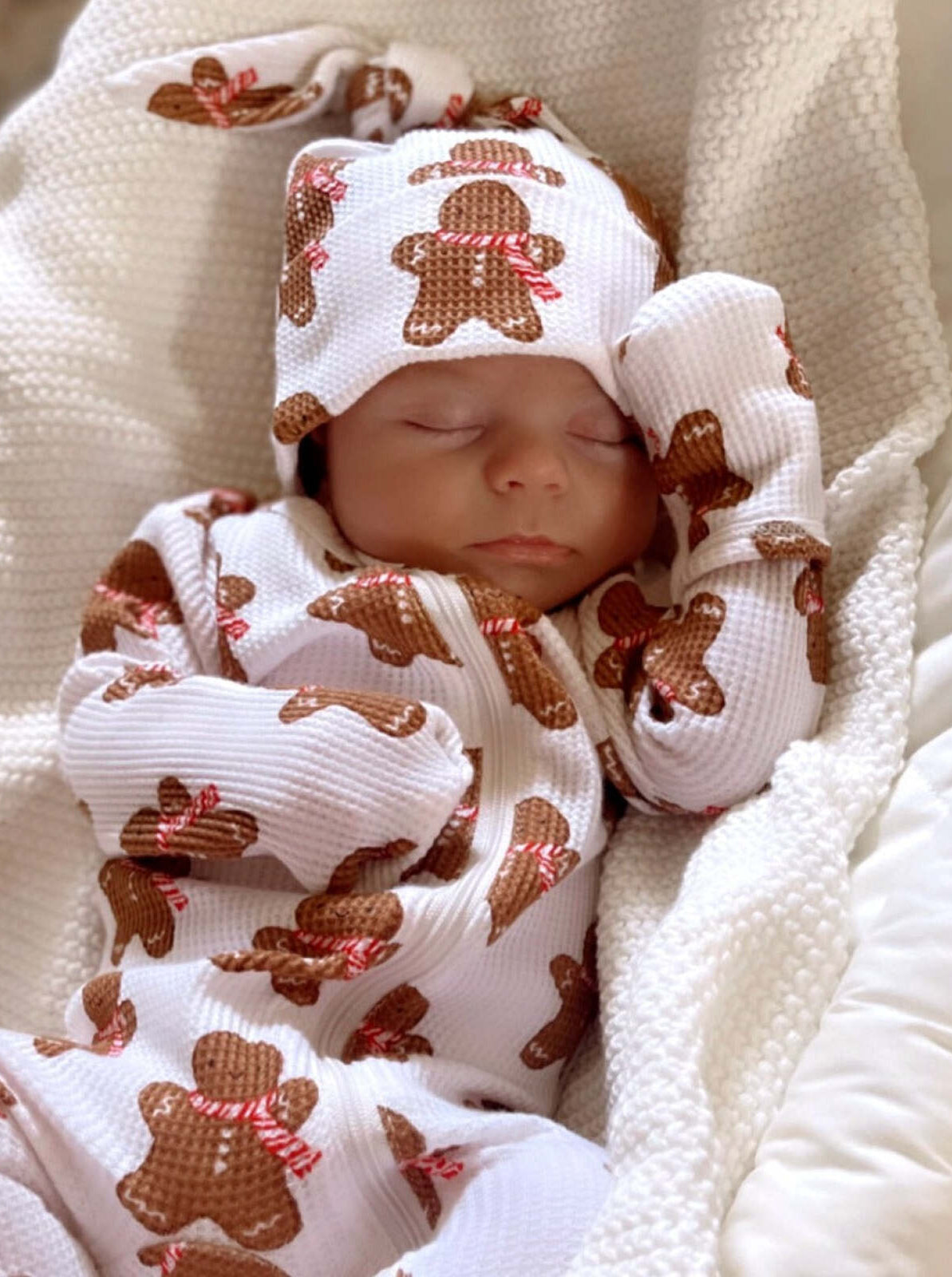 Sleeping baby wearing a gingerbread-themed outfit, snuggled in a soft blanket.