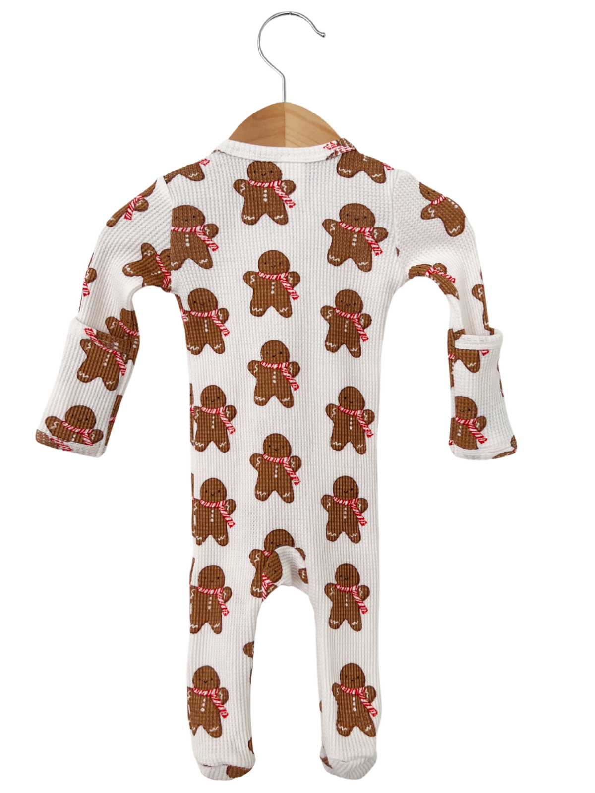 Gingerbread-patterned baby onesie hanging on a wooden hanger.