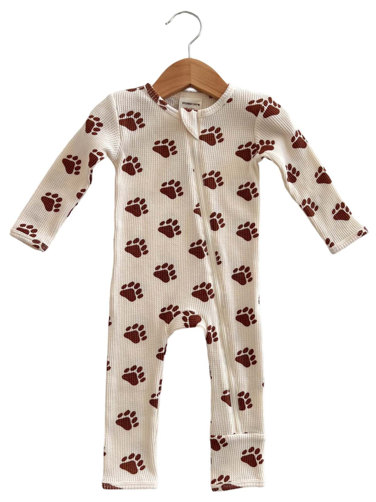 Children's one-piece pajama with brown paw print pattern, hung on a wooden hanger against a neutral background.