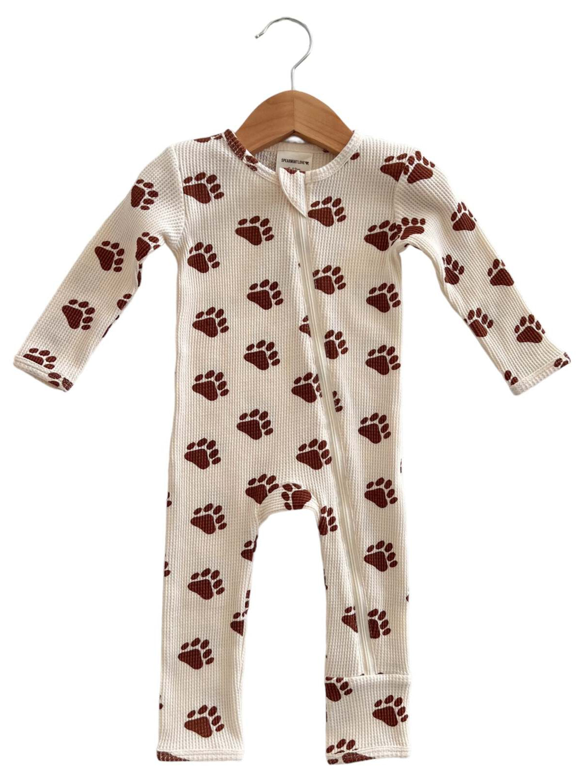 Children's one-piece pajama with brown paw print pattern, hung on a wooden hanger against a neutral background.