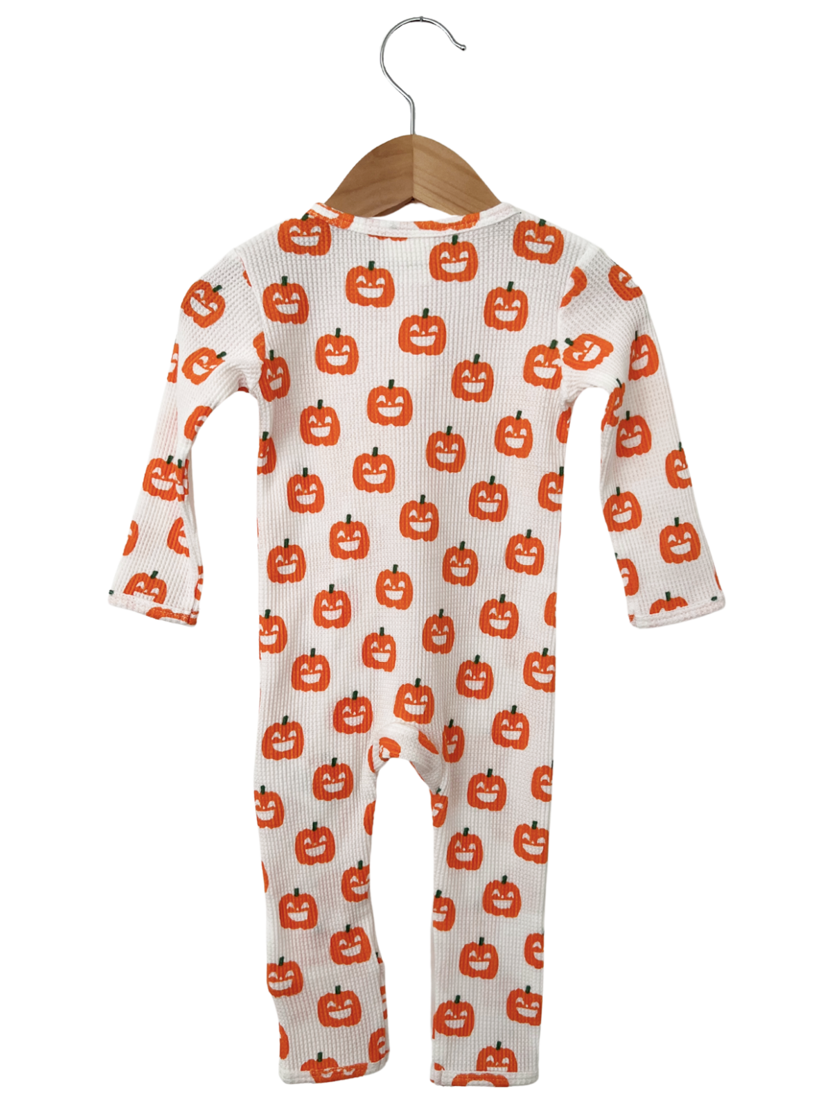 Children's long-sleeve onesie featuring a pattern of smiling orange pumpkins on a white background, hung on a wooden hanger.