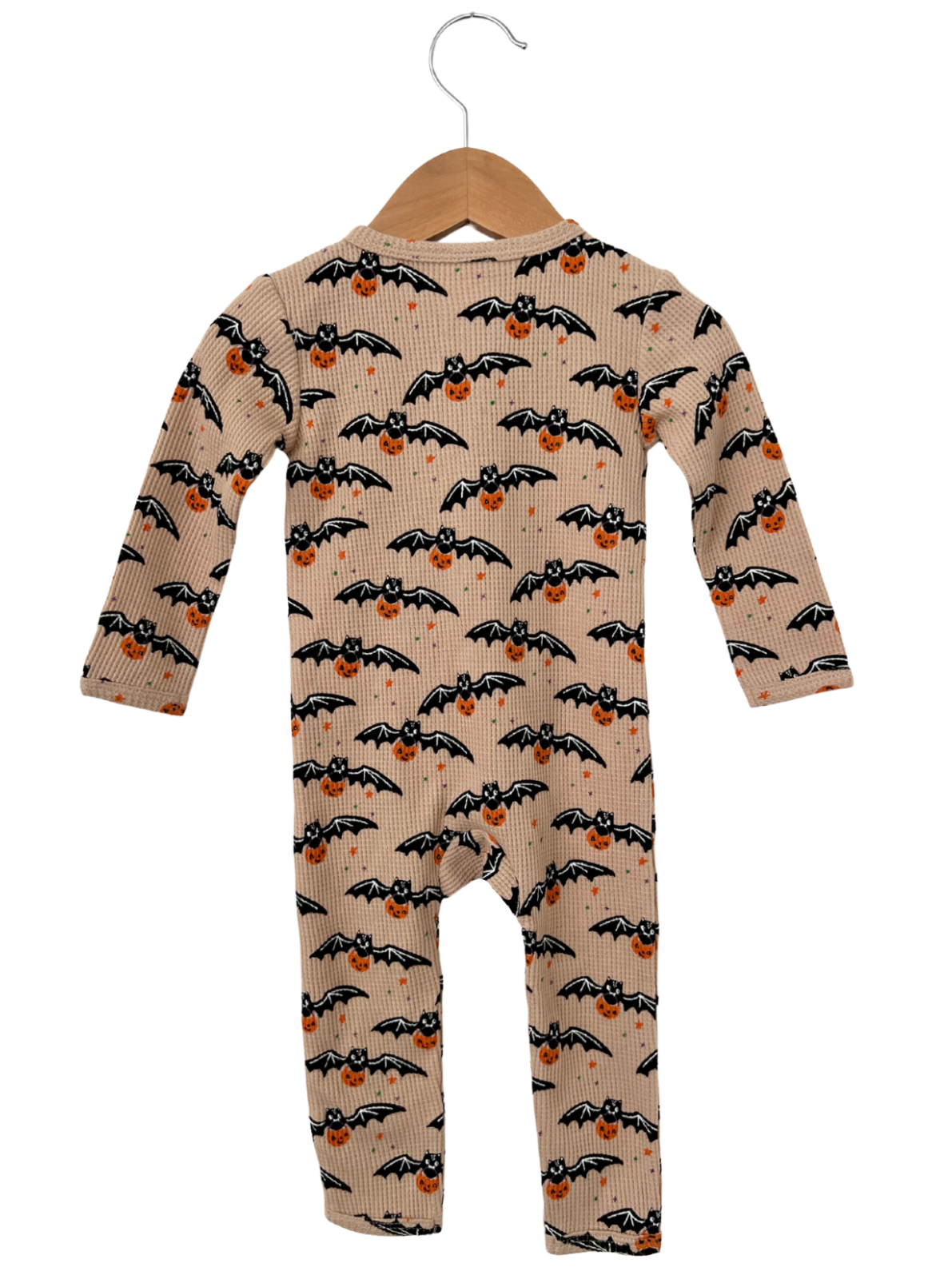 Tan baby onesie with a playful print of bats and pumpkins hanging on a wooden hanger.