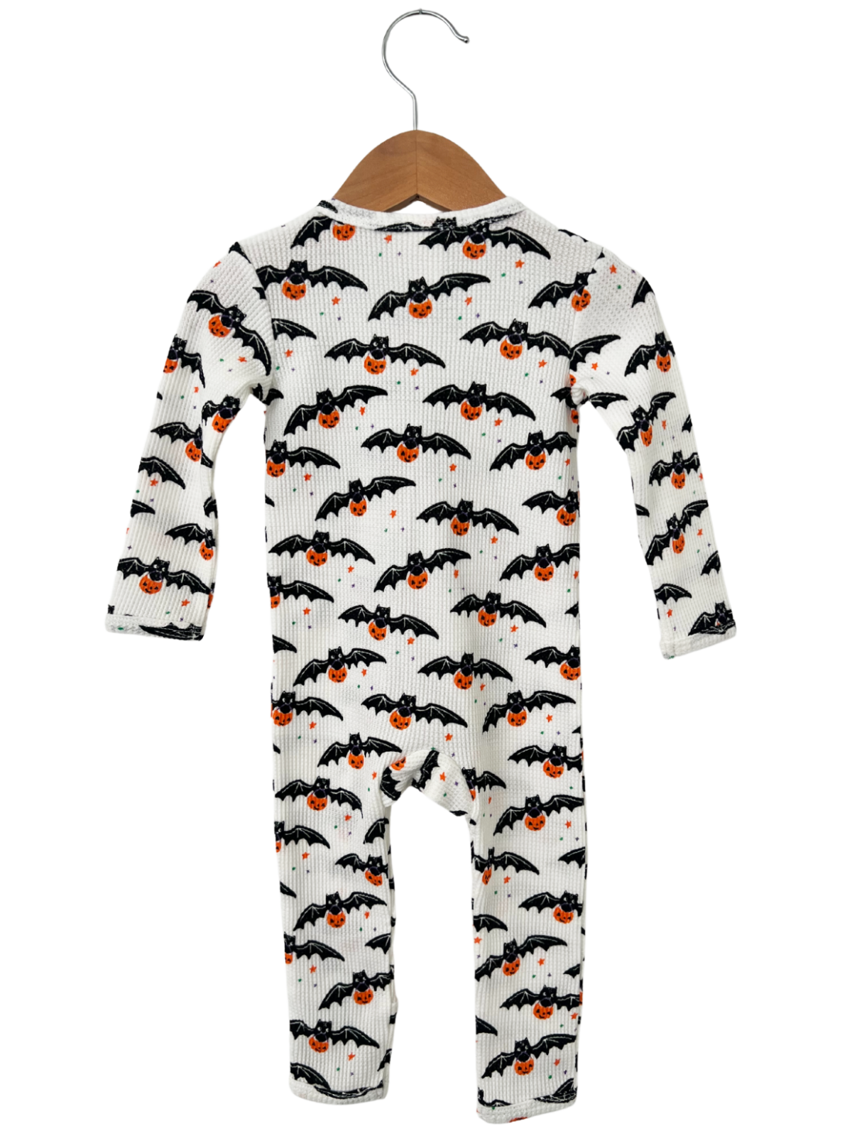 Baby onesie with black bats and orange pumpkins on a white background, hanging on a wooden hanger.