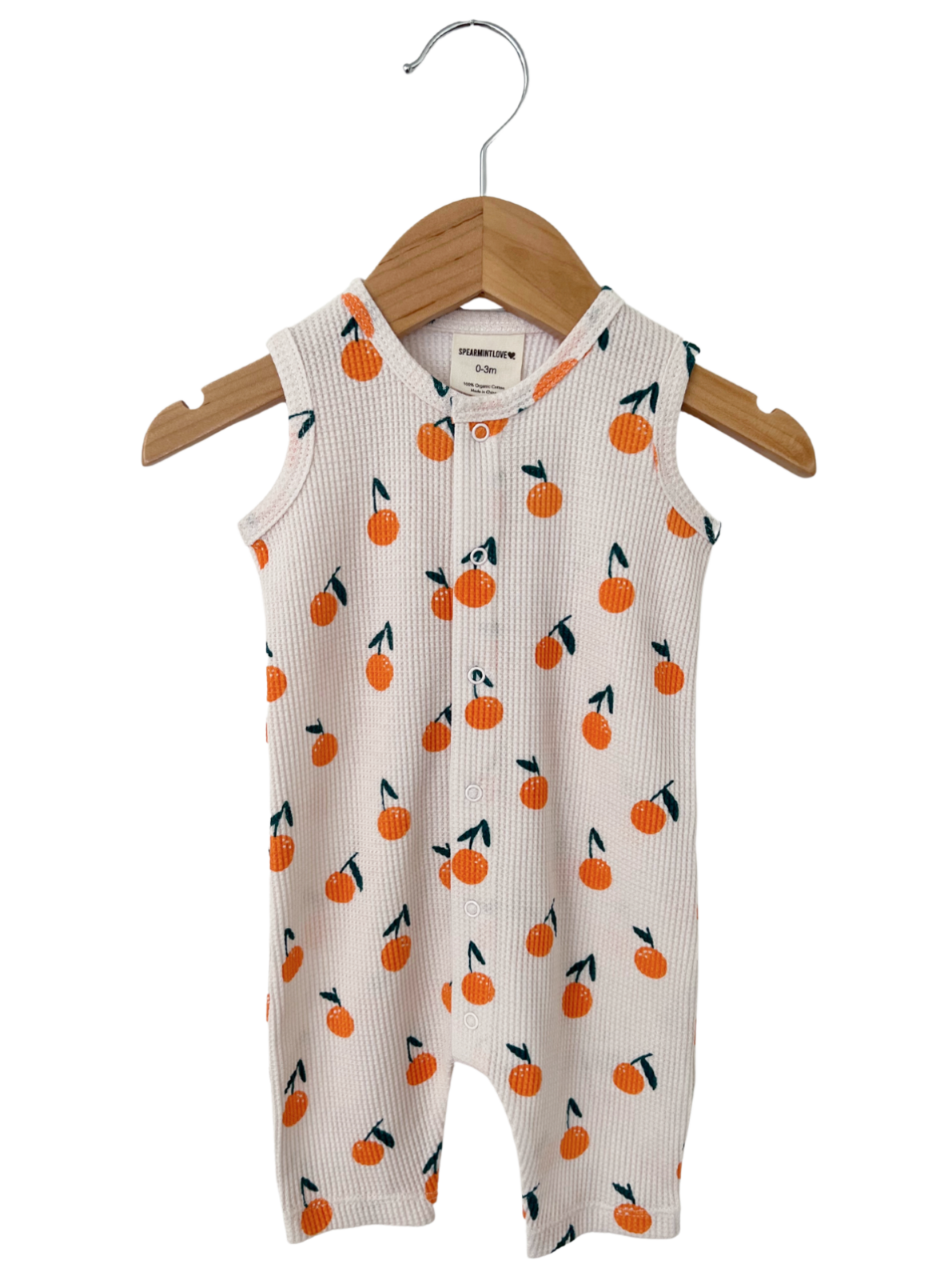 White baby romper with orange fruit pattern, hanging on a wooden hanger. Perfect for infants.