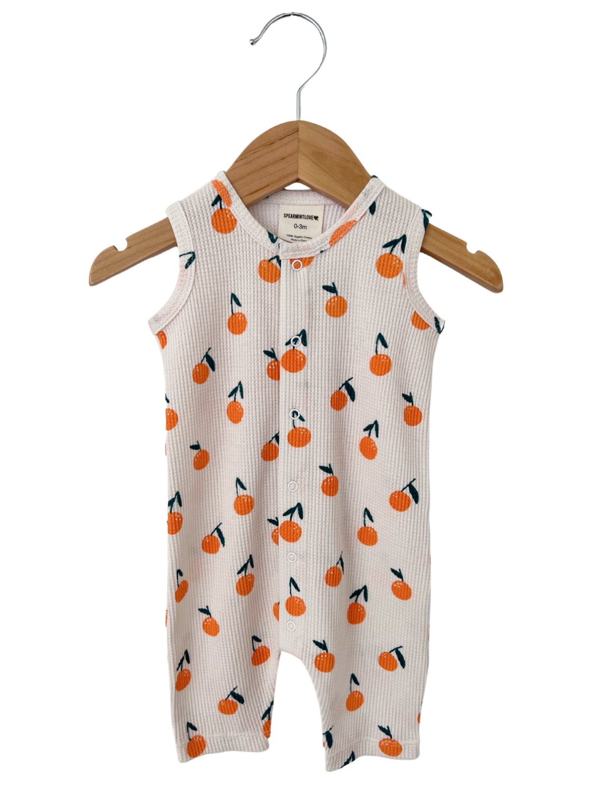 White baby romper with orange fruit pattern, hanging on a wooden hanger. Perfect for infants.