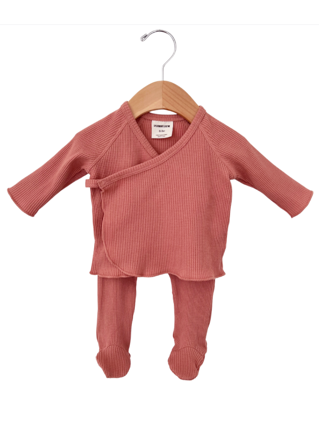 Pink ribbed baby outfit displayed on a wooden hanger, featuring a wrap top and matching pants.