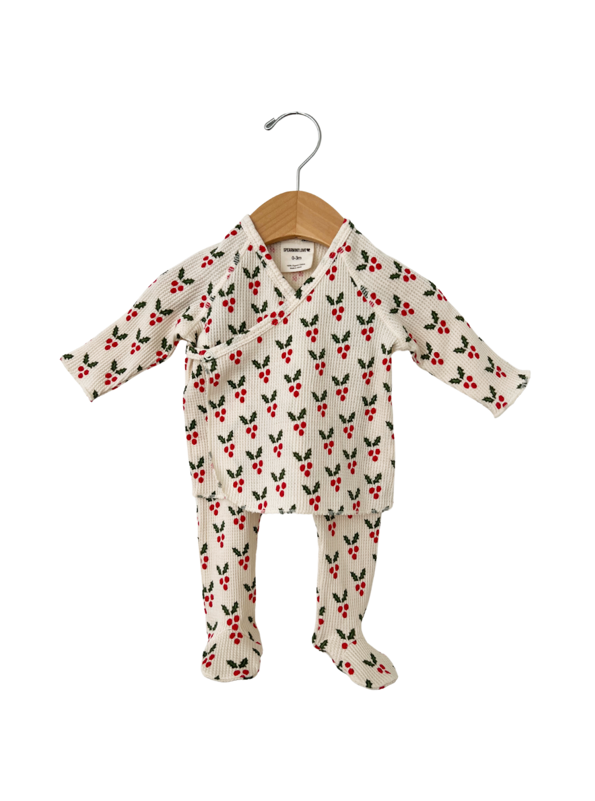 White baby outfit with red cherry pattern, hanging on a wooden hanger.