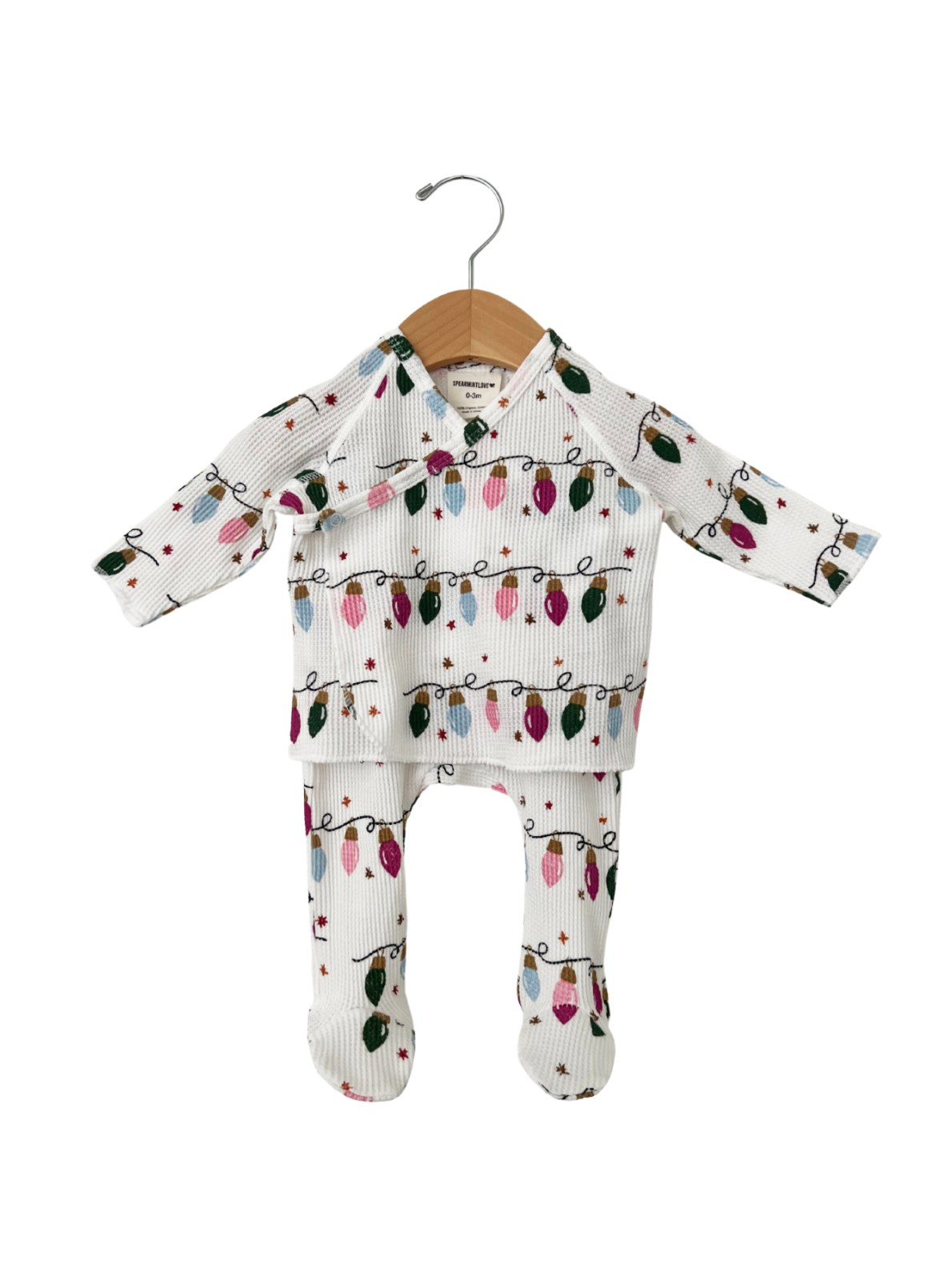 White baby outfit with festive light bulb pattern, including a long-sleeve top and matching pants, hanging on a wooden hook.