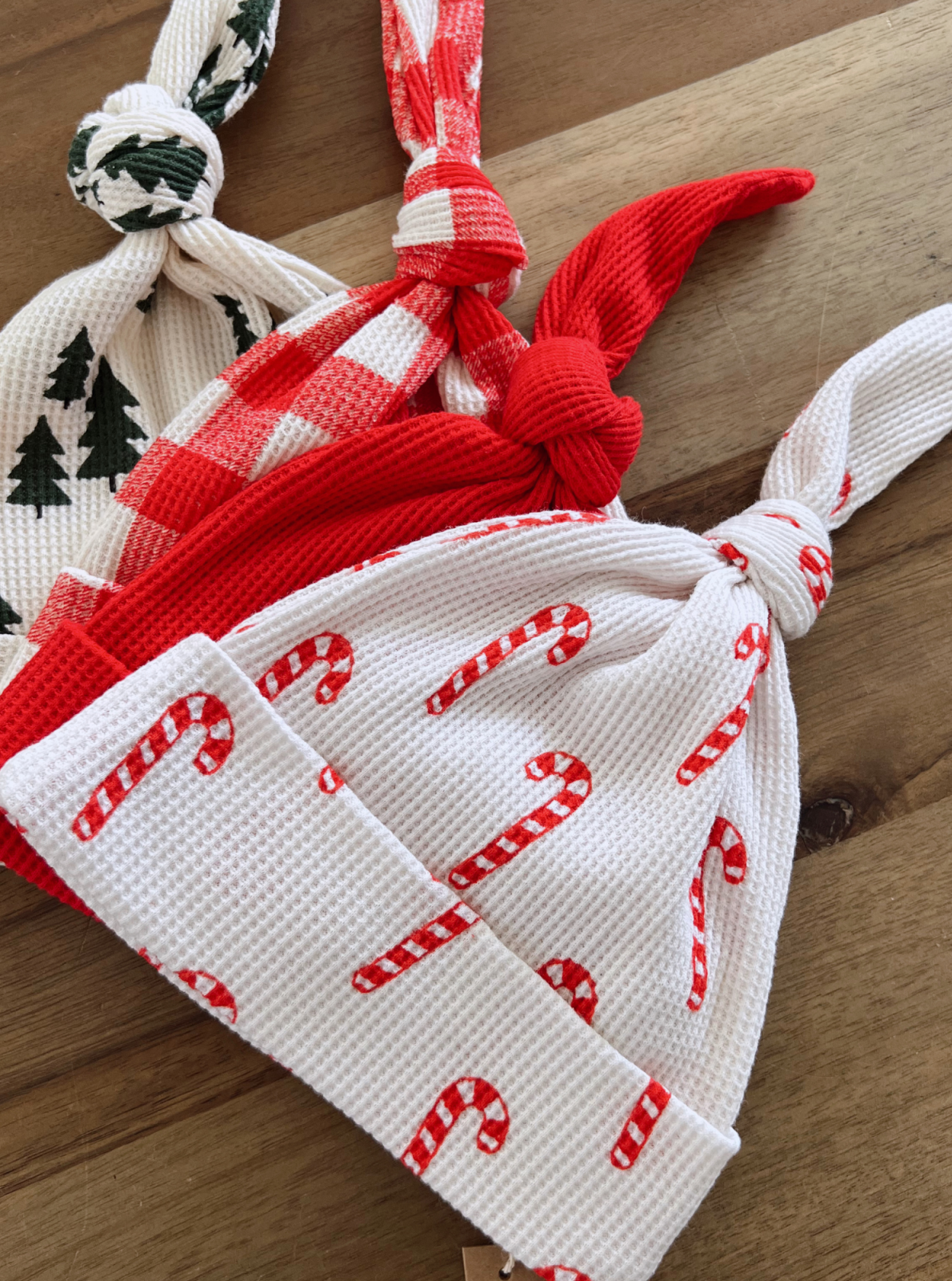 Three festive hats in red and white with candy cane and plaid patterns, displayed on a wooden surface.