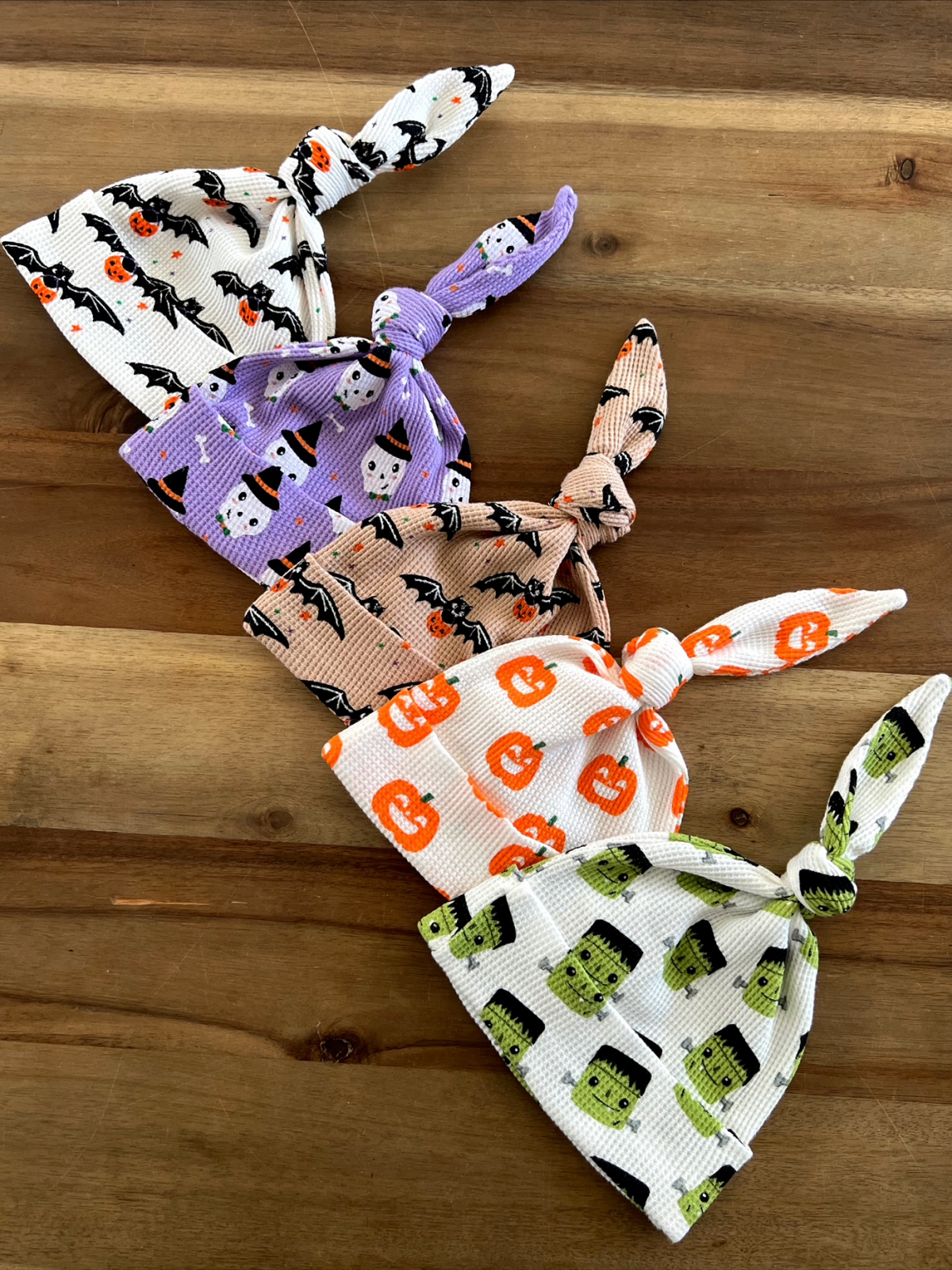Five Halloween-themed baby hats with various designs on a wooden surface.