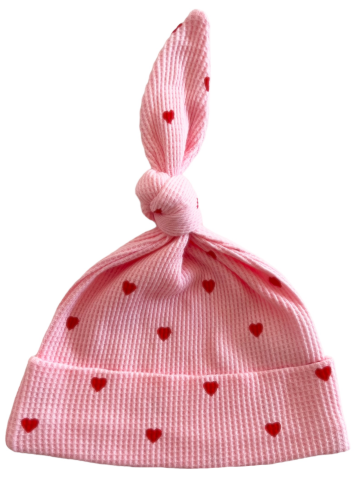Pink knit baby hat with red heart patterns and a knot on top.