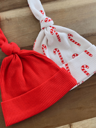 Red and white patterned baby hats with candy cane design, tied at the top, on a wooden surface.