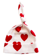 White baby beanie with red heart and polka dot patterns, featuring a cute knot on top.