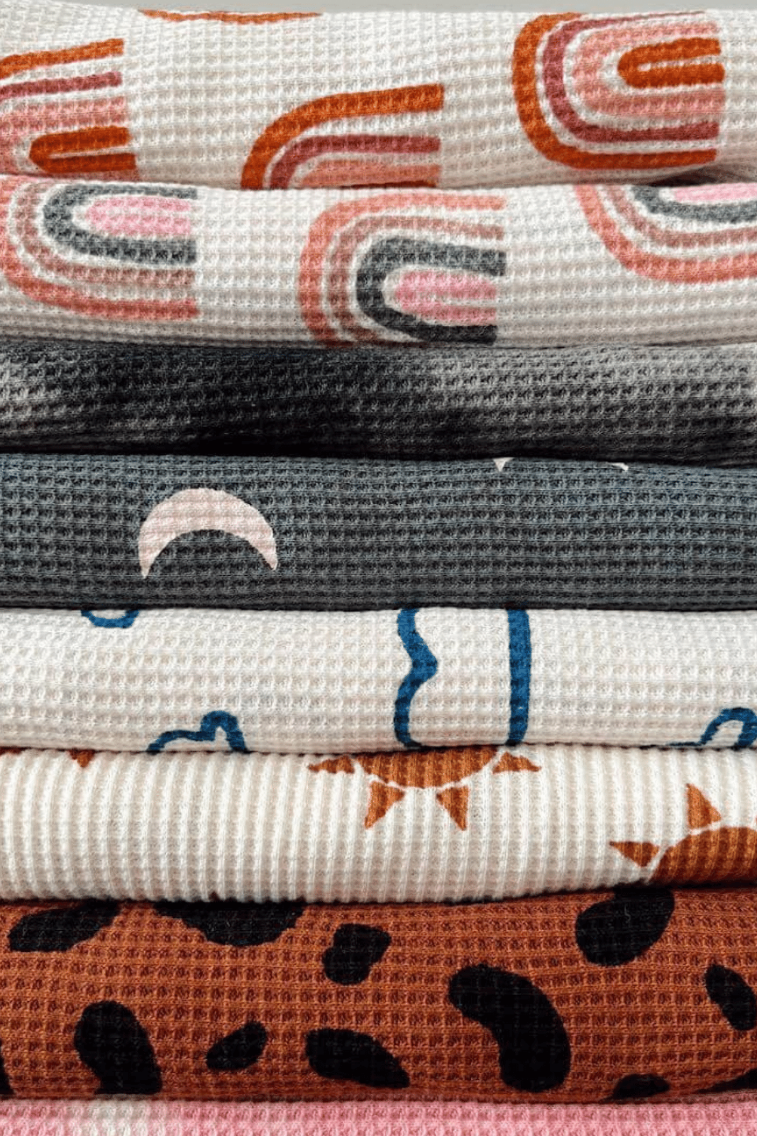 Stack of patterned fabric with designs including rainbows, moons, and leopard prints in various colors and textures.