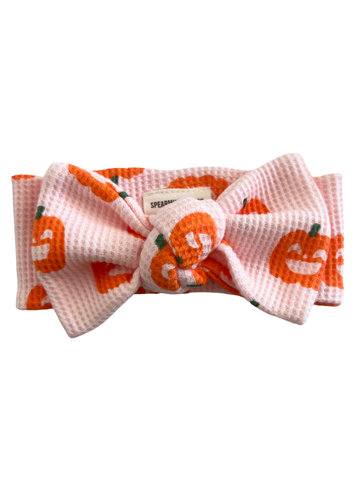 Pink headband with orange pumpkin prints and a large bow. Ideal for autumn or festive occasions.