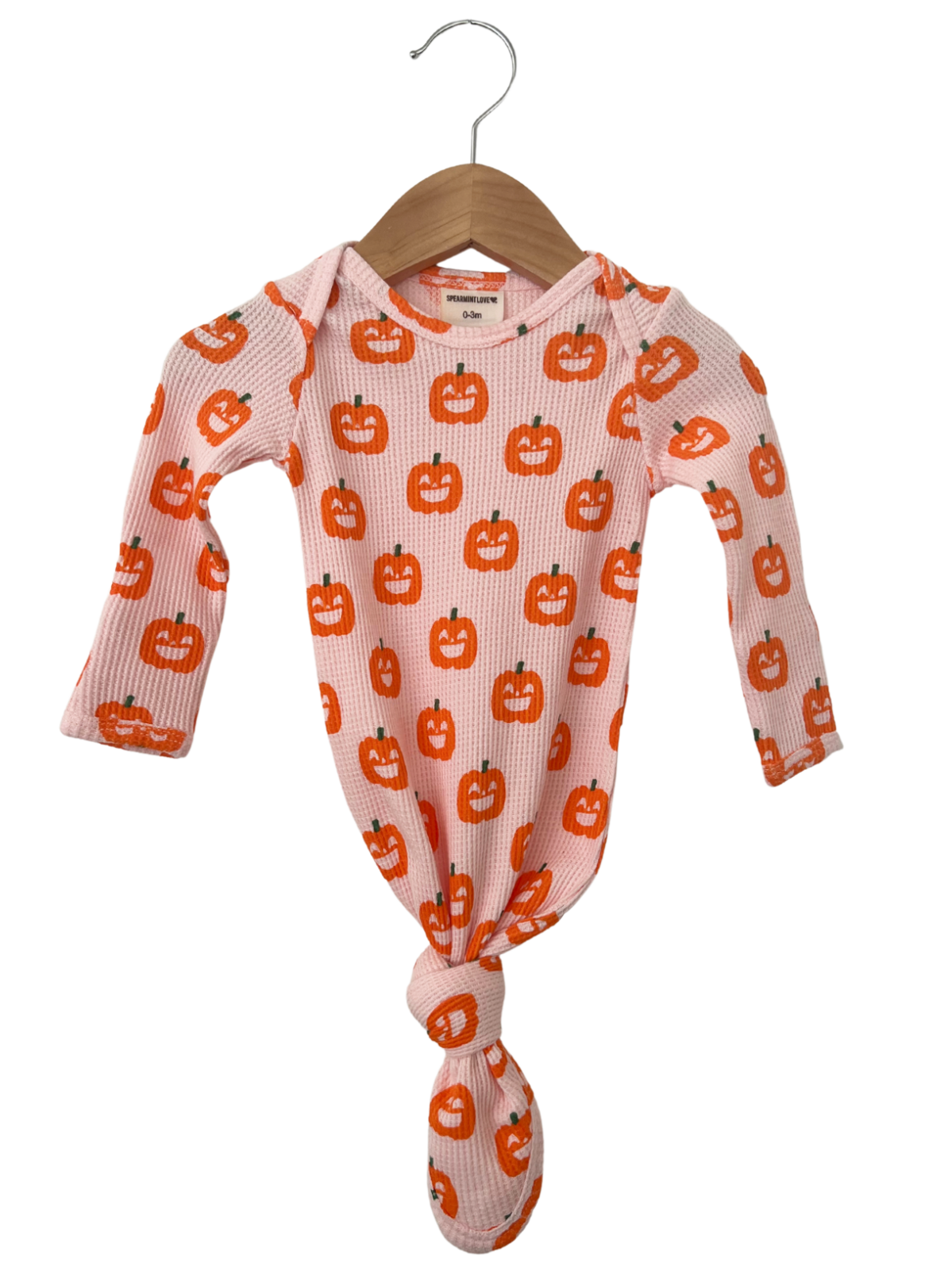 Infant bodysuit with orange pumpkin prints, tied at the bottom, hanging on a wooden hanger against a white background.