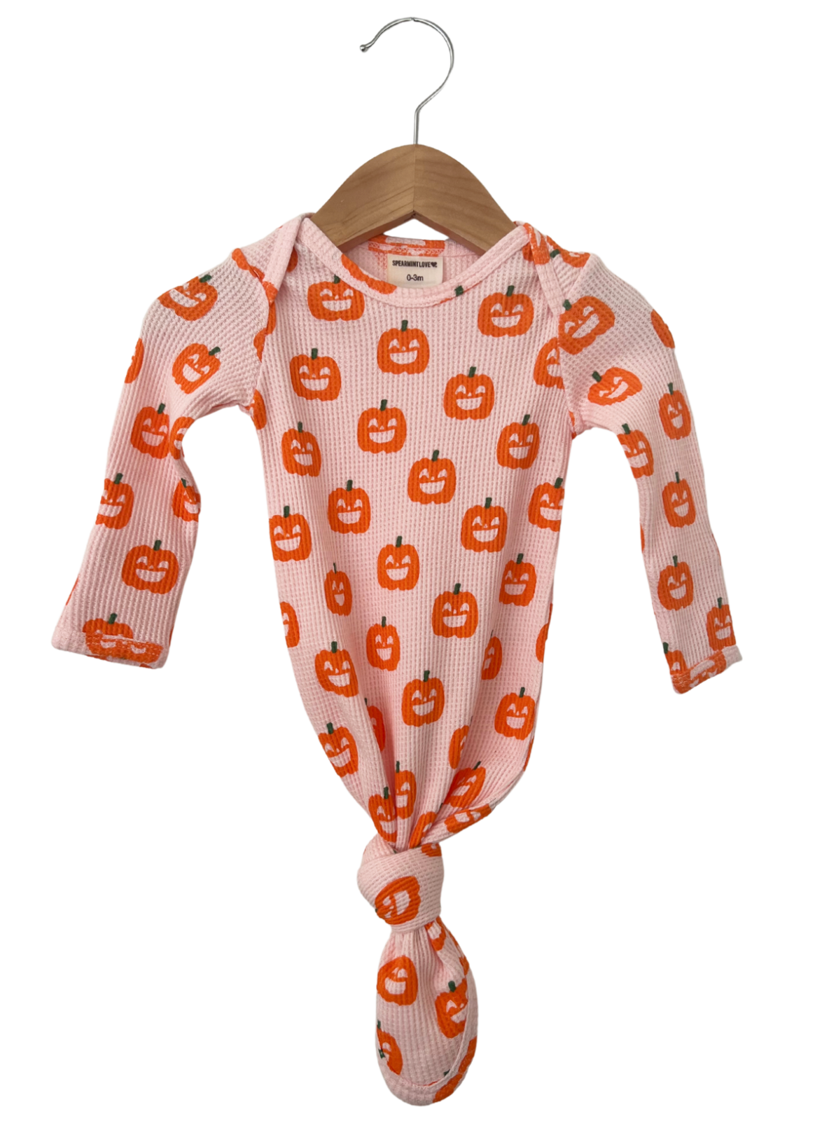 Infant bodysuit with orange pumpkin prints, tied at the bottom, hanging on a wooden hanger against a white background.