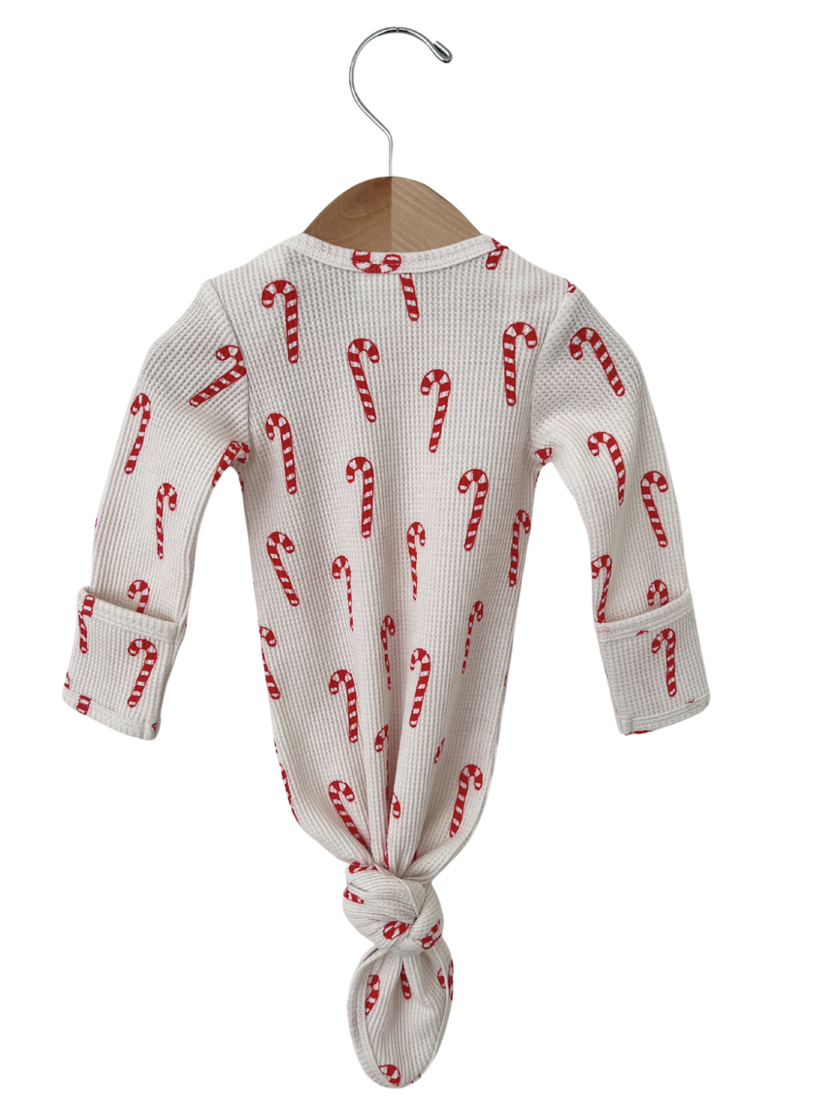 White long-sleeve onesie with red candy cane pattern, tied at the bottom, hanging on a wooden hanger.