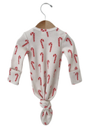 White long-sleeve onesie with red candy cane pattern, tied at the bottom, hanging on a wooden hanger.