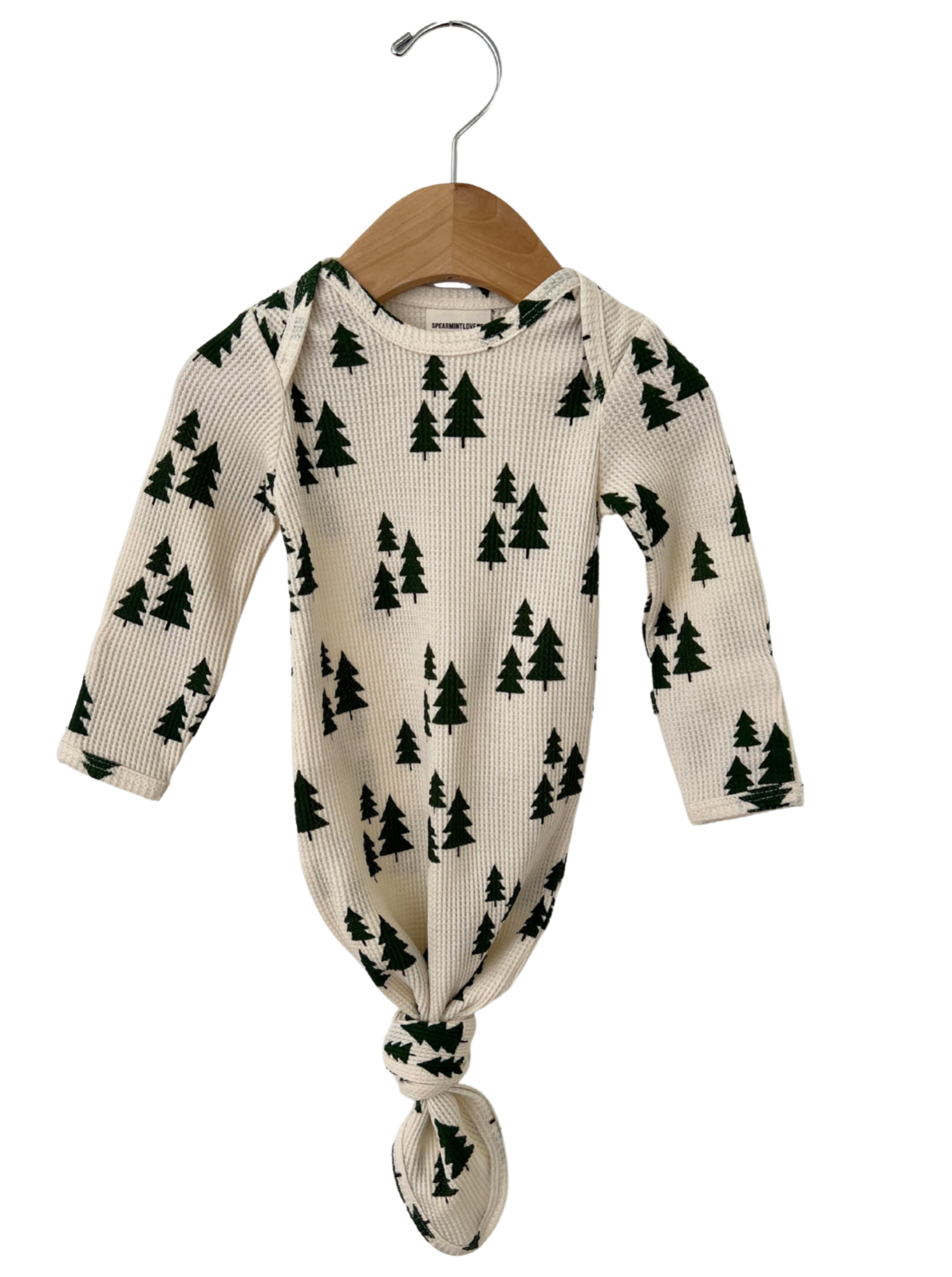 Cream-colored infant outfit with green tree pattern, hung on a wooden hanger.