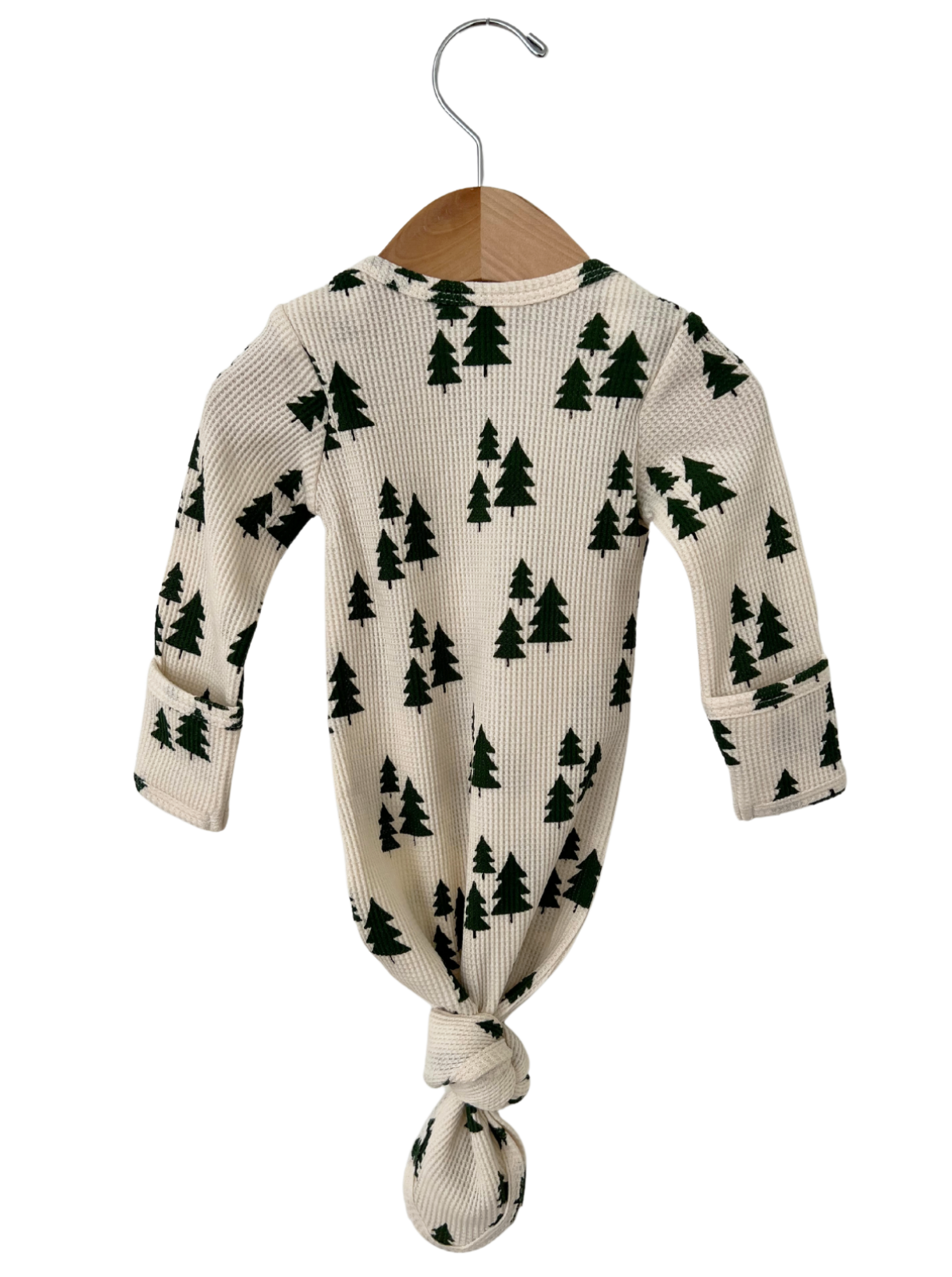 Knotted infant outfit hanging on a wooden hanger, featuring a cream background with green tree patterns.