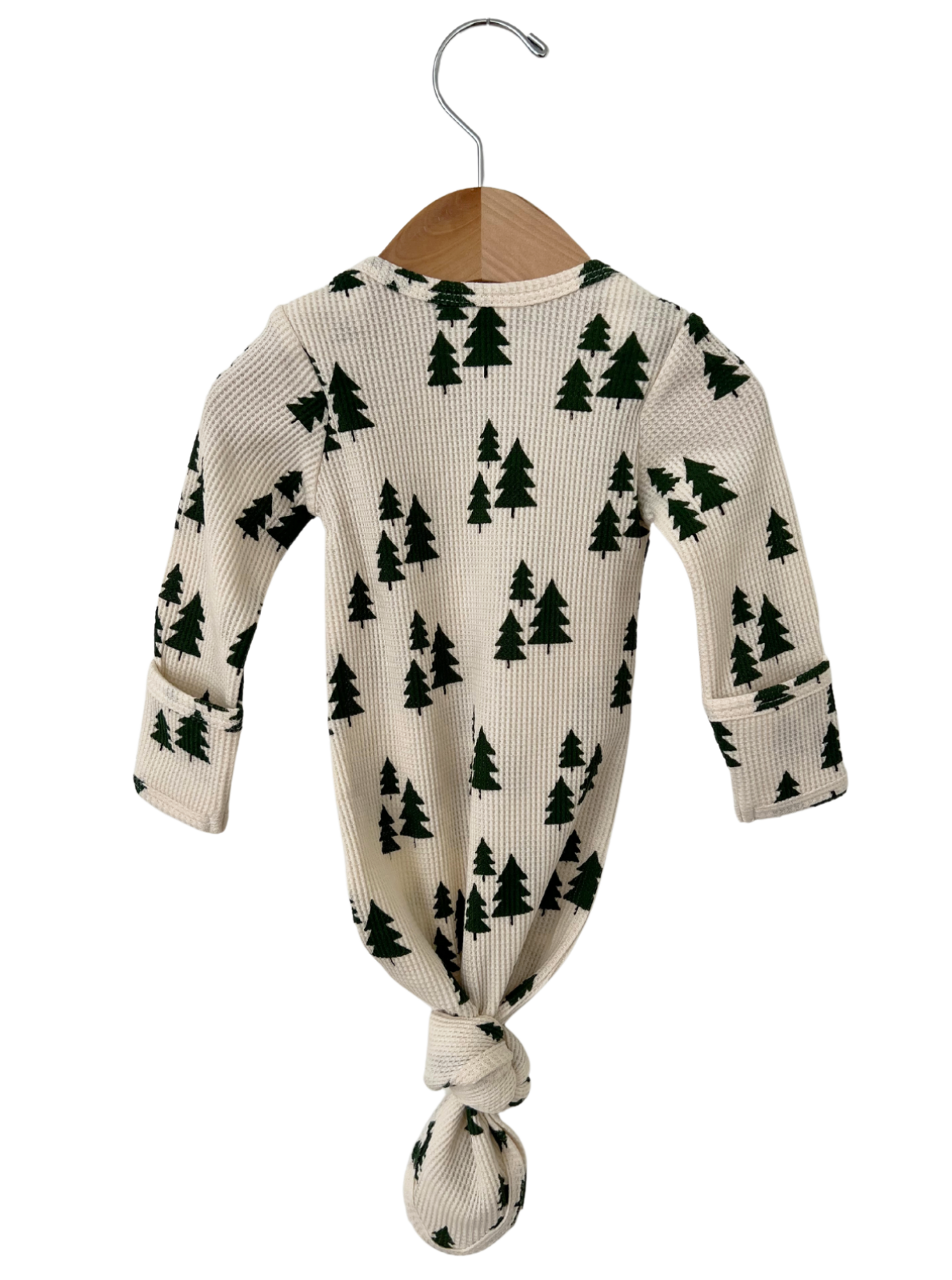 Knotted infant outfit hanging on a wooden hanger, featuring a cream background with green tree patterns.