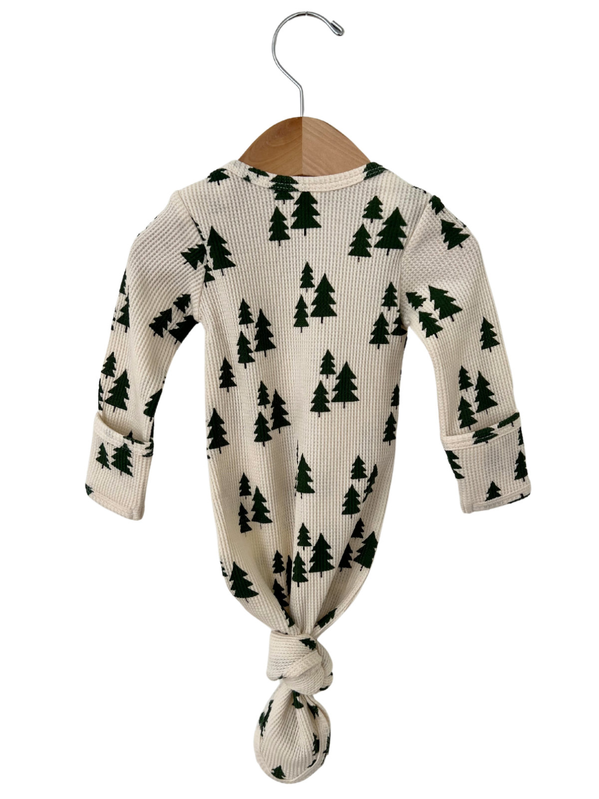 Knotted infant outfit hanging on a wooden hanger, featuring a cream background with green tree patterns.