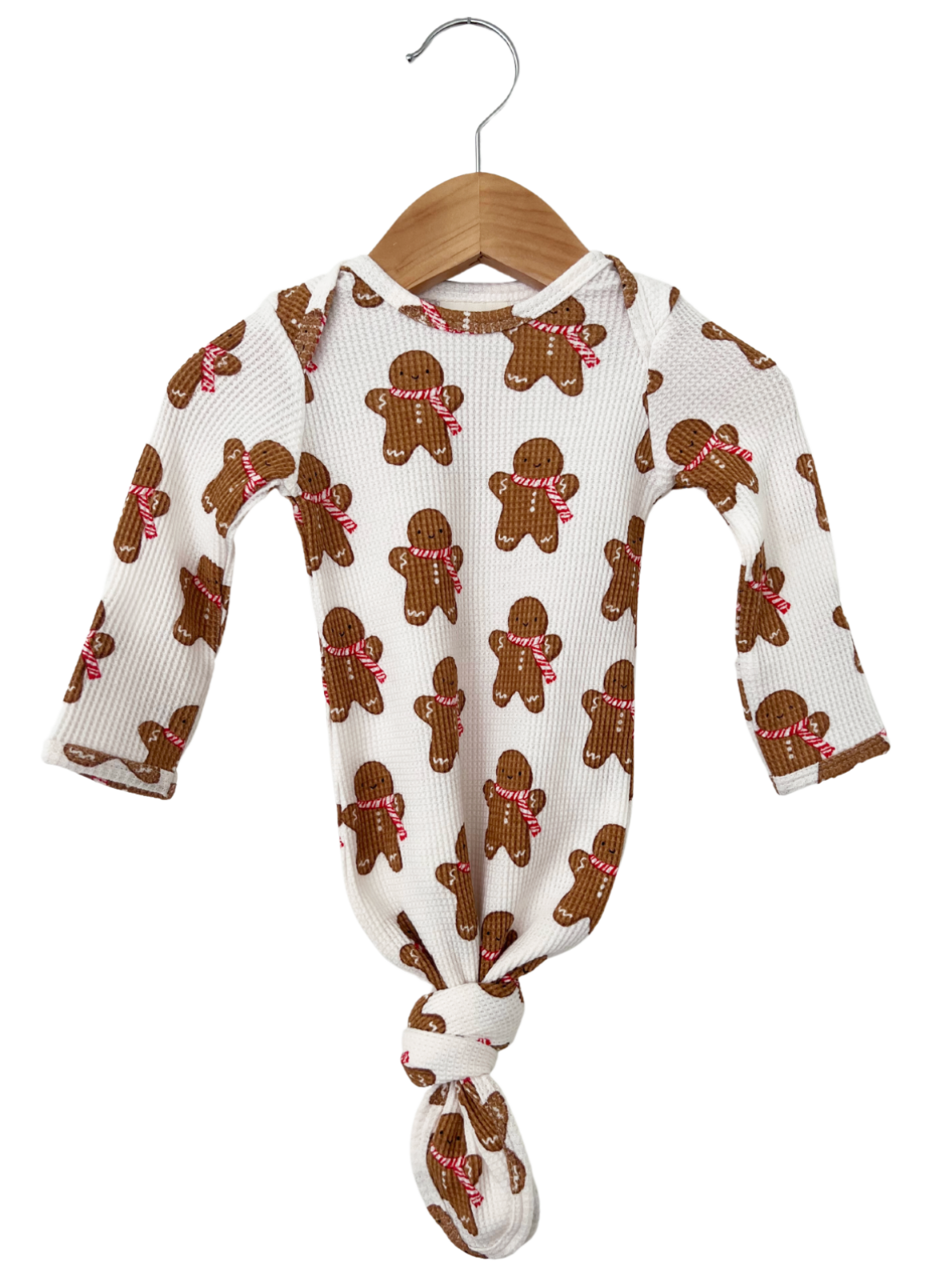 Infant onesie with gingerbread cookie pattern, featuring long sleeves and a knotted bottom, displayed on a wooden hanger.
