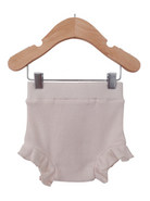 Light pink baby shorts with ruffles, hanging on a wooden hanger against a white background.