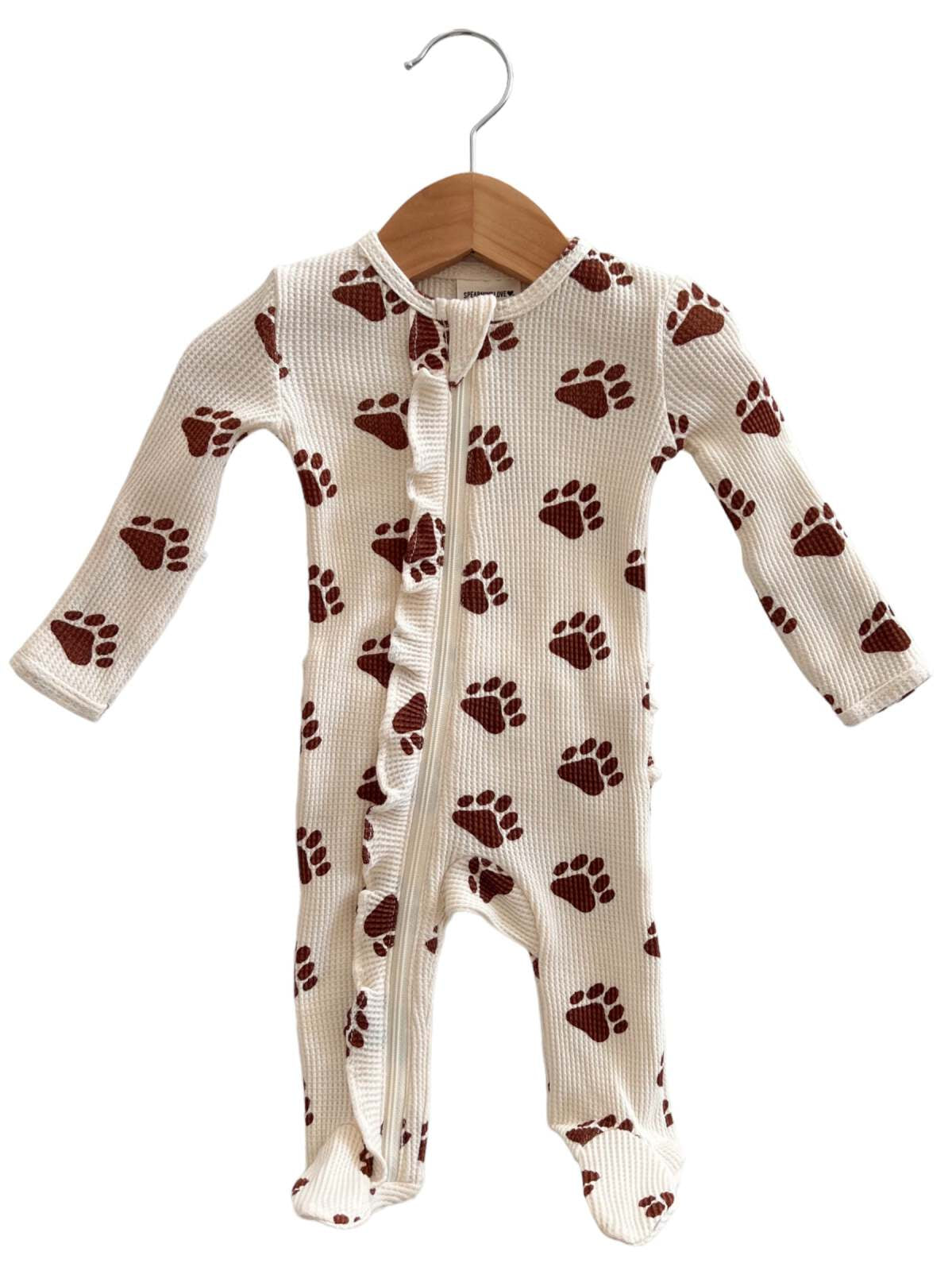 White onesie with brown paw print pattern, hanging on a wooden hanger. Suitable for infants or toddlers.