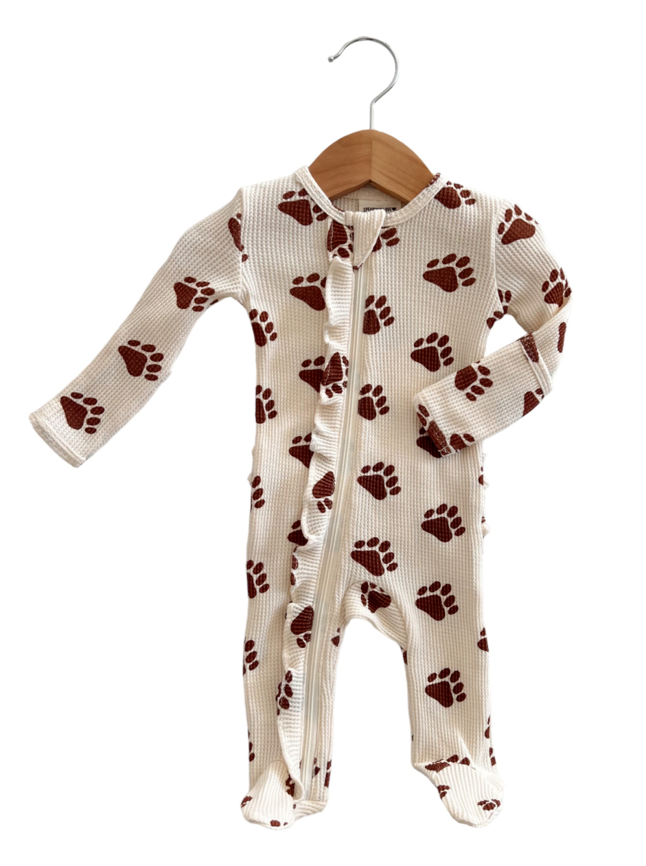 White baby onesie with red paw prints, displayed on a wooden hanger against a plain background.