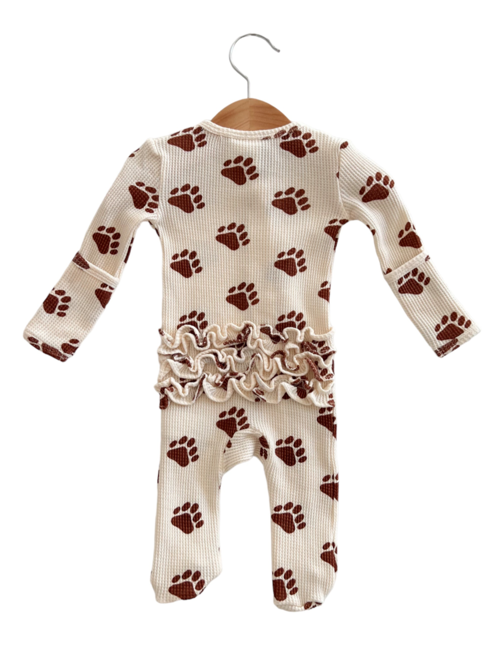 Cream-colored baby onesie with brown paw prints and ruffled waist, hanging on a wooden hanger.