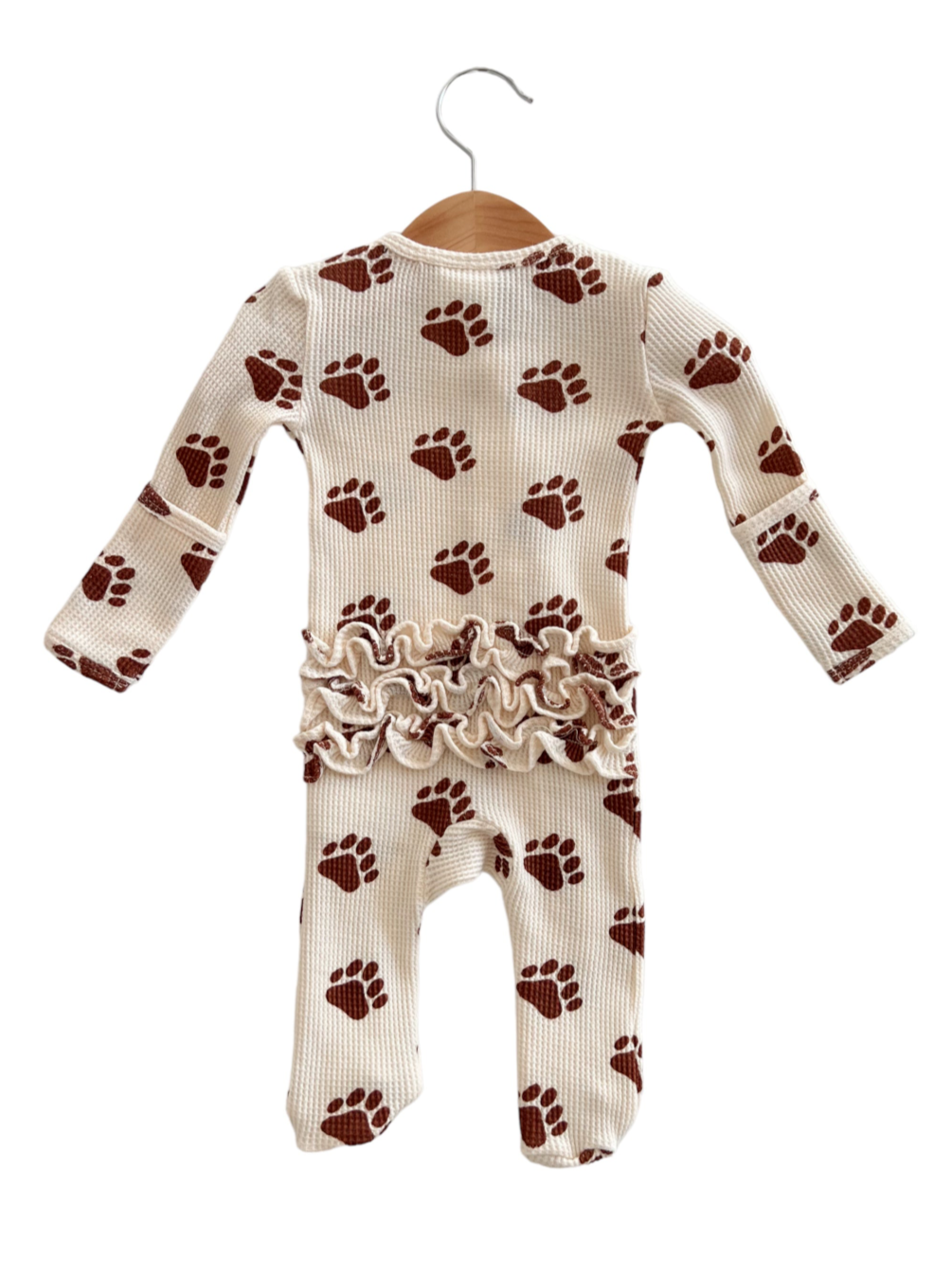 Cream-colored baby onesie with brown paw prints and ruffled waist, hanging on a wooden hanger.