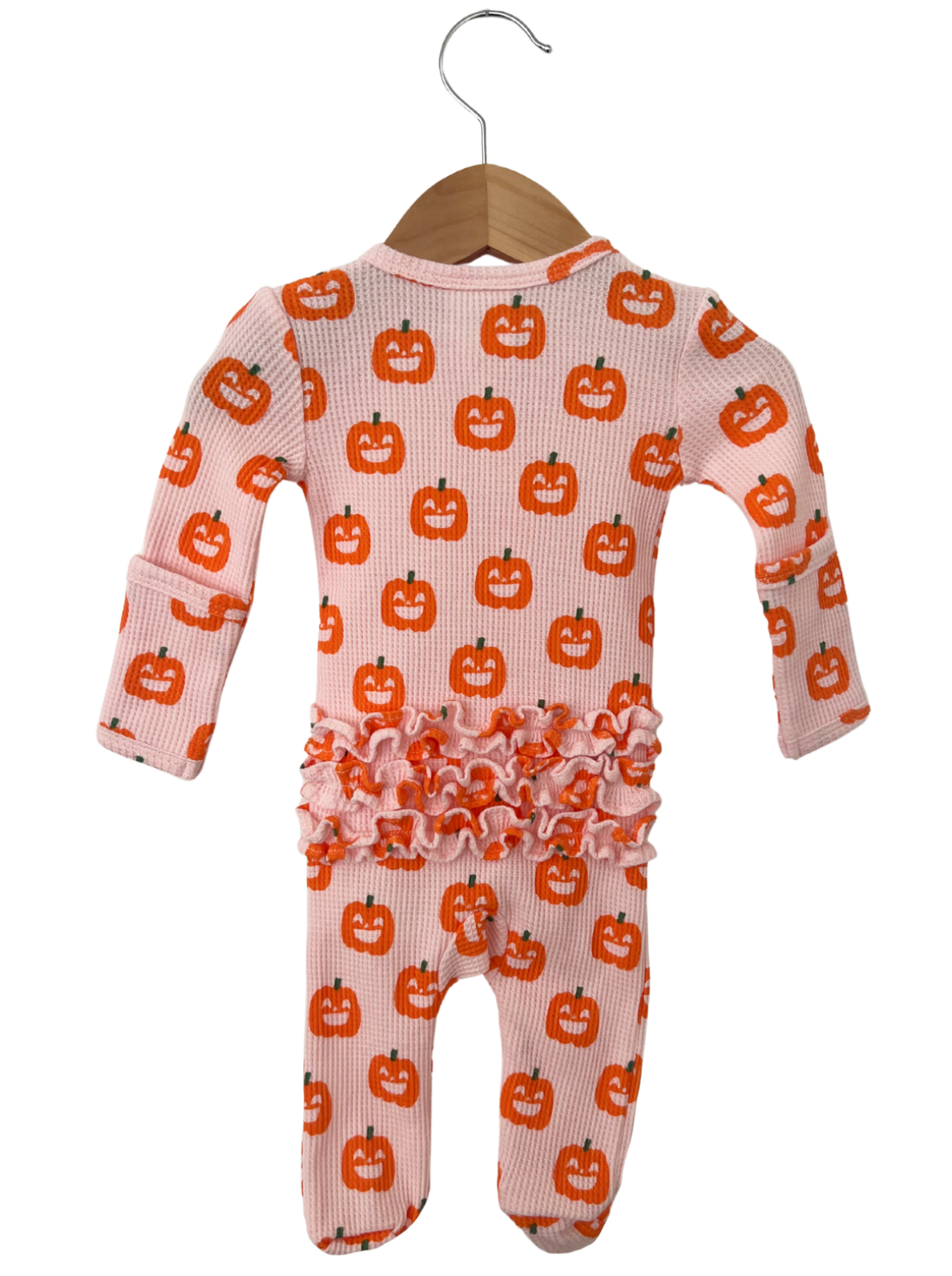 Pink baby onesie with pumpkin patterns and ruffles, hanging on a wooden hanger against a white background.