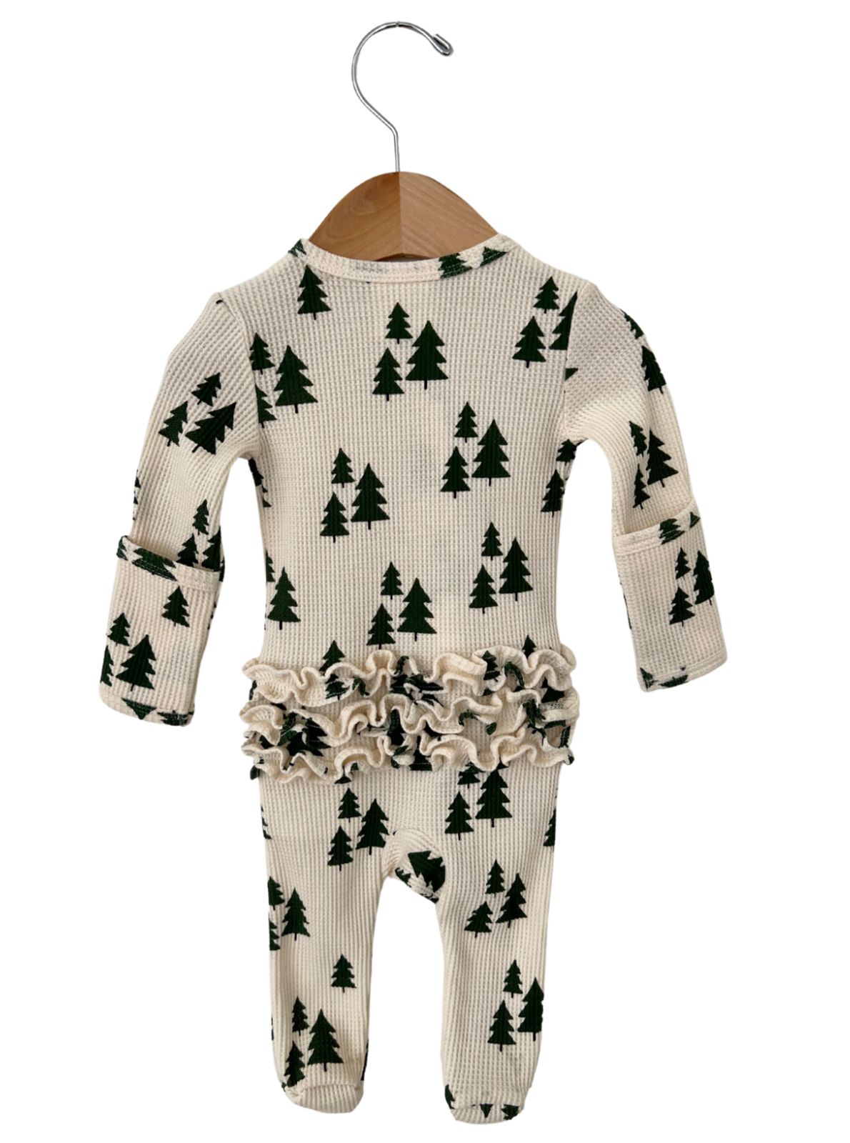 Cream-colored infant onesie with green tree print and ruffled waistband, hanging on a wooden hanger.