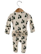 Cream-colored infant onesie with green tree print and ruffled waistband, hanging on a wooden hanger.