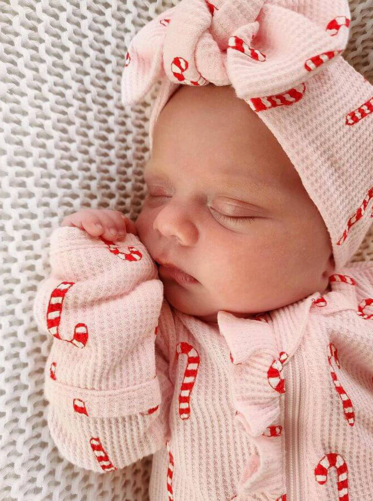 Sleeping baby in pink outfit with candy cane design, wearing a matching headband, peacefully resting.