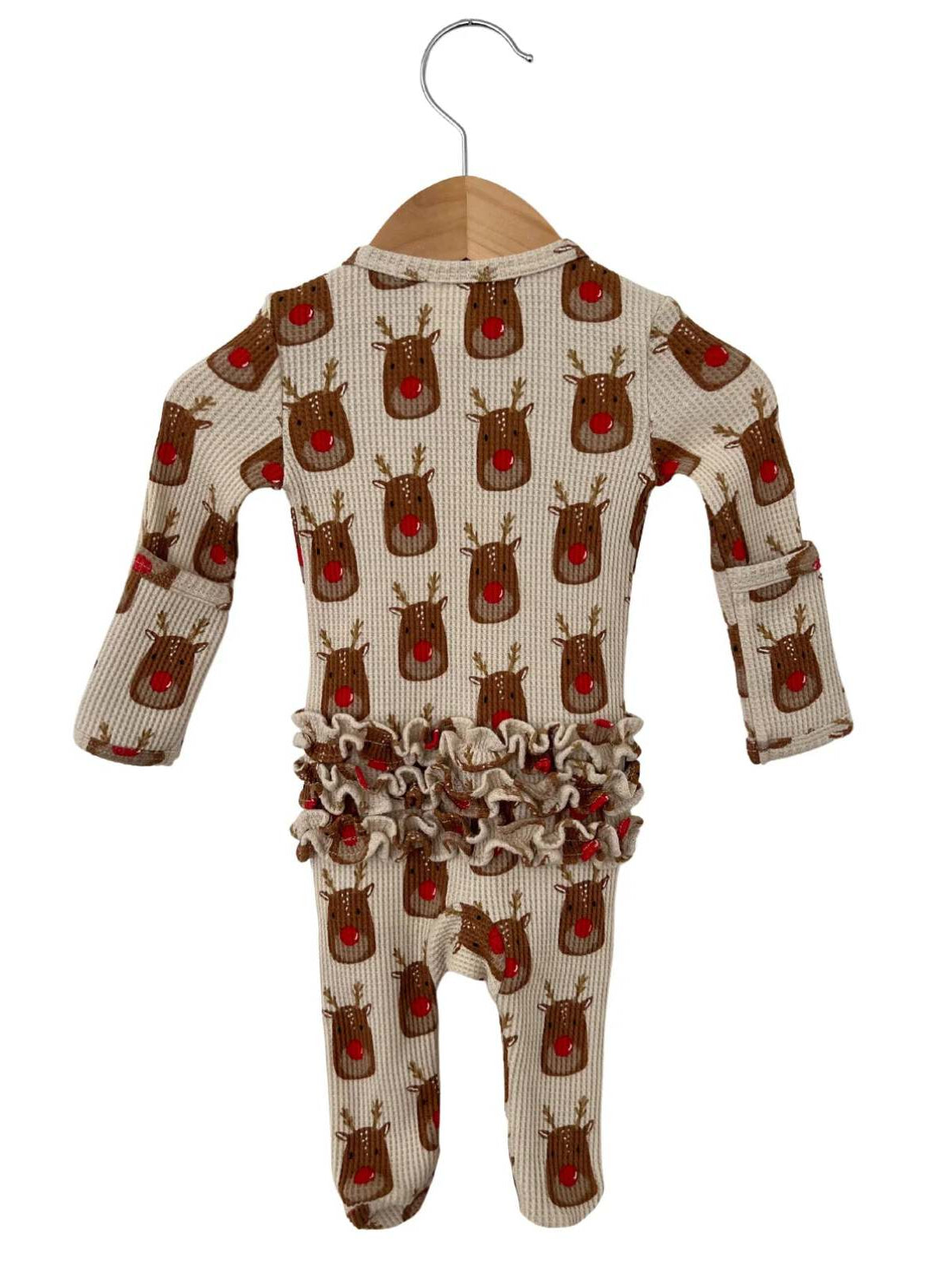 Cream-colored onesie with reindeer pattern and ruffled waist, displayed on a wooden hanger.